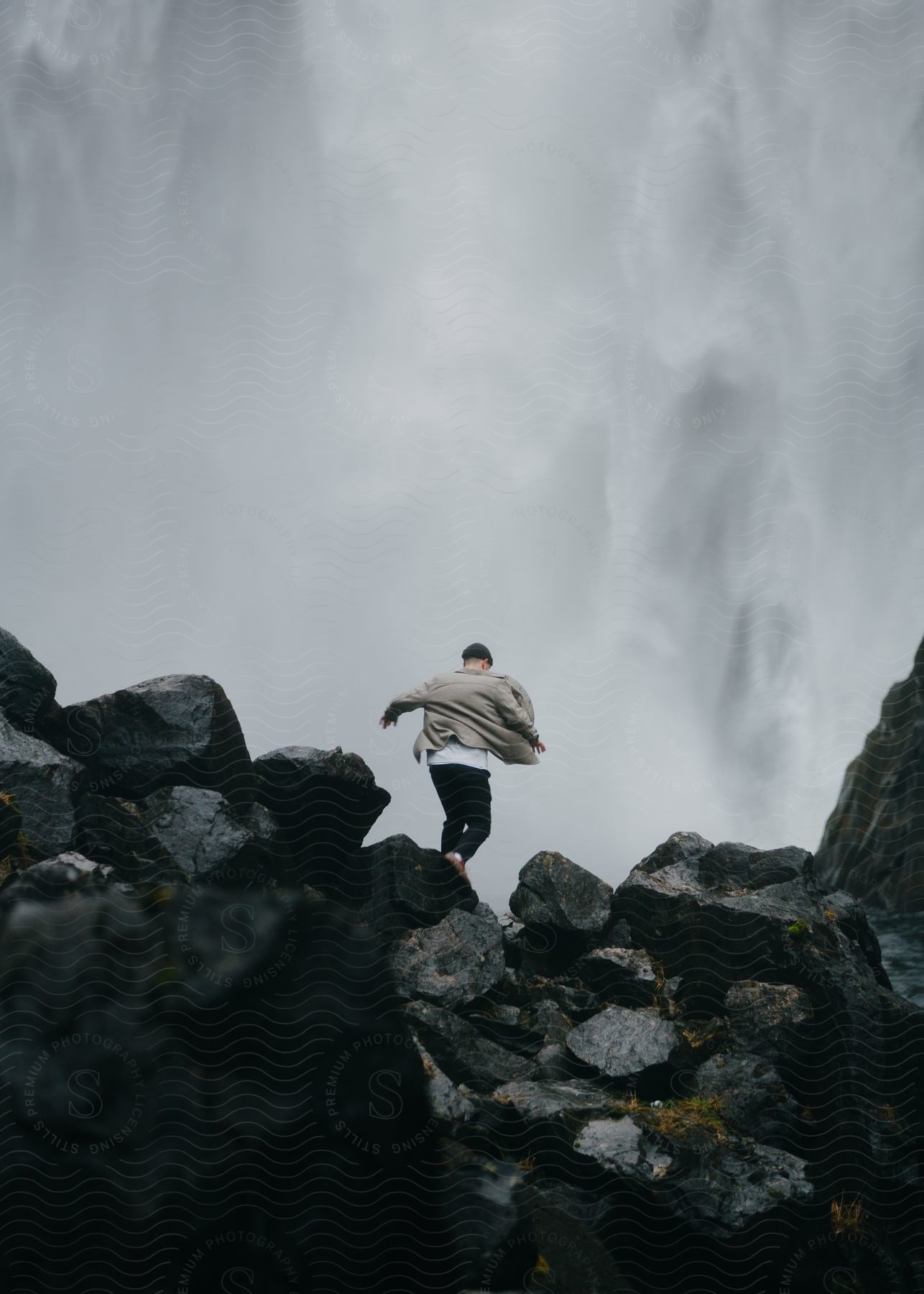 A determined man runs across sharp rocks towards a gray sky with his jacket blowing in the wind