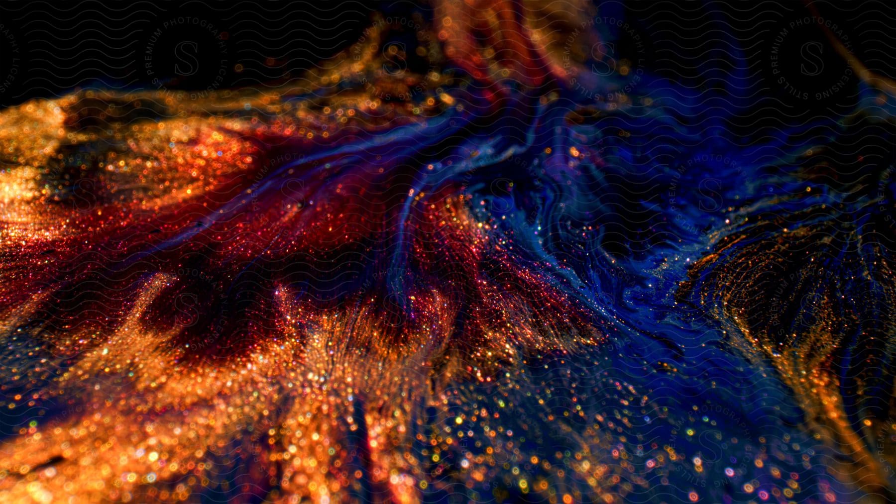 Red and orange glitter glows on a dark shiny liquid surface