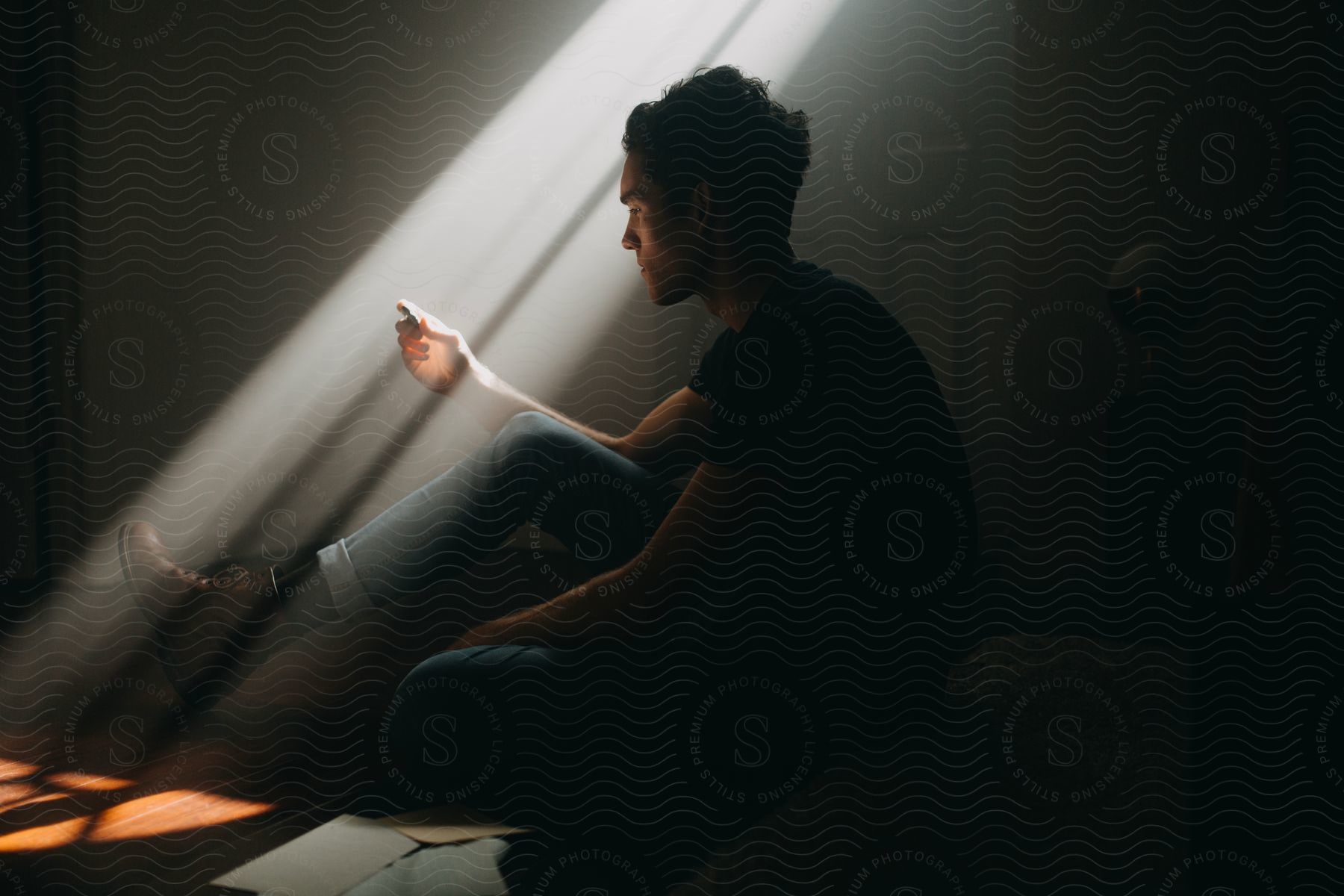 A person sitting on the floor in a darkened room with a ray of light shining down