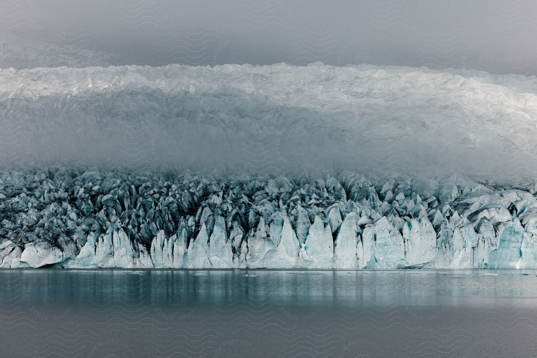 Jagged ice meets the ocean with snow mounds behind on a cloudy day