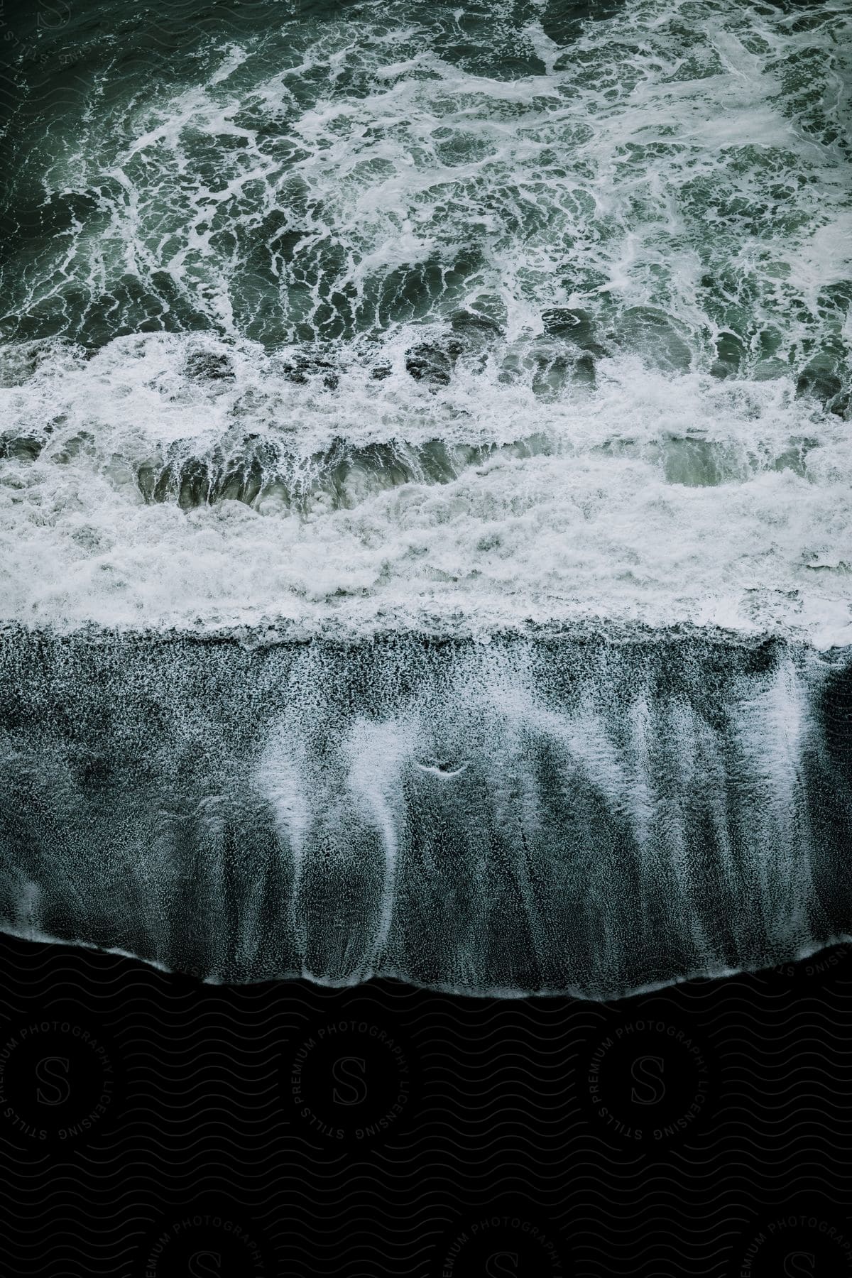 Aerial shot of ocean waves crashing against a black sand beach