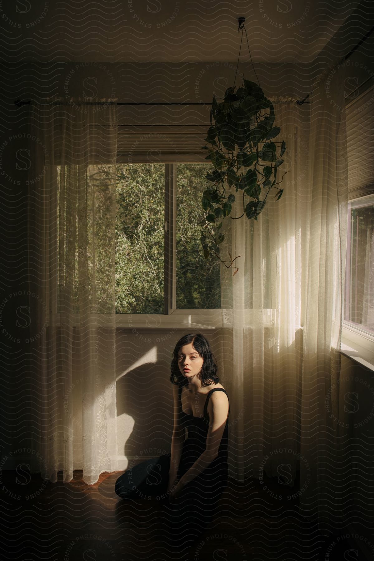 A young woman with dark hair sitting on the floor next to a window