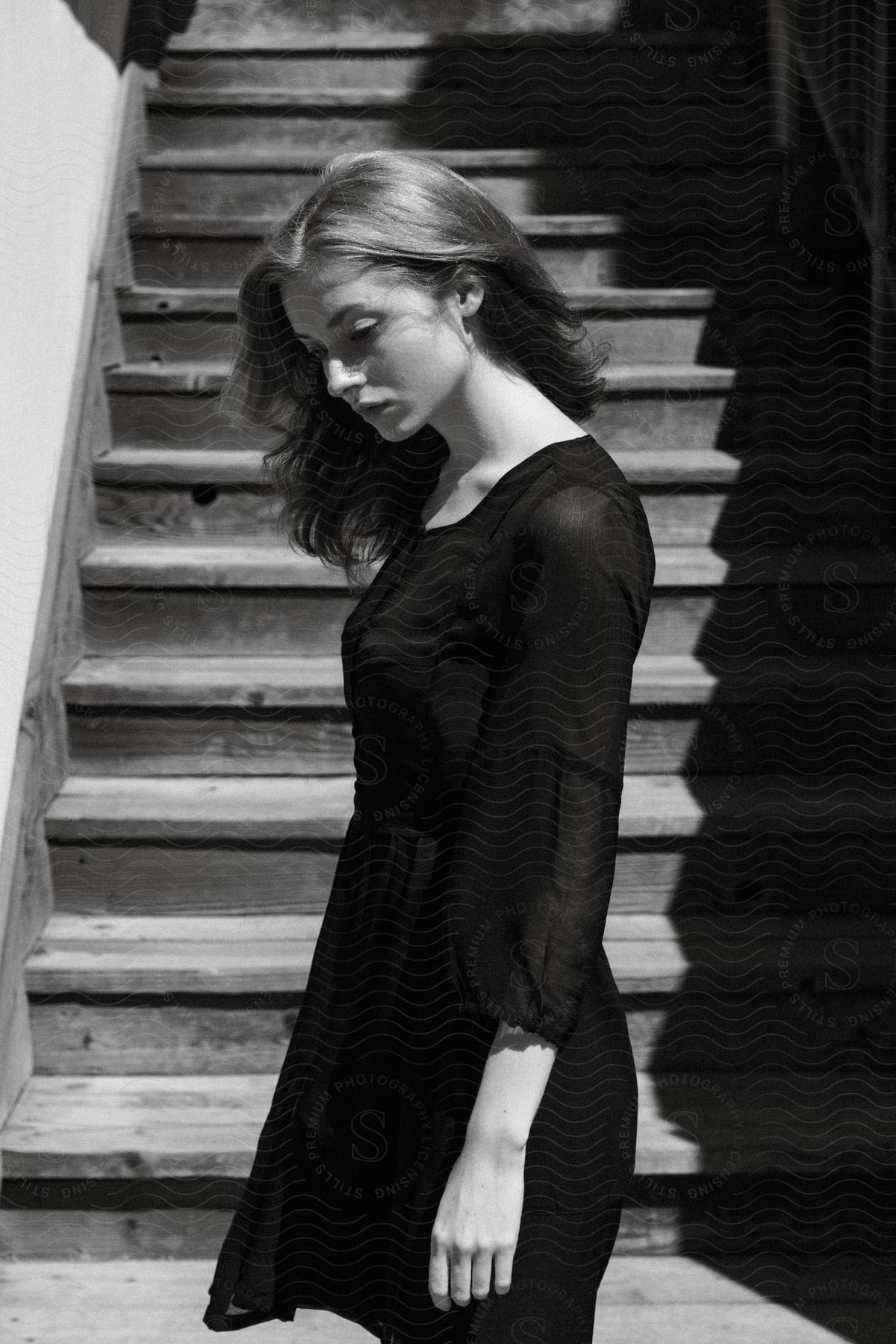 A young woman standing outdoors in front of a staircase looking down at the ground