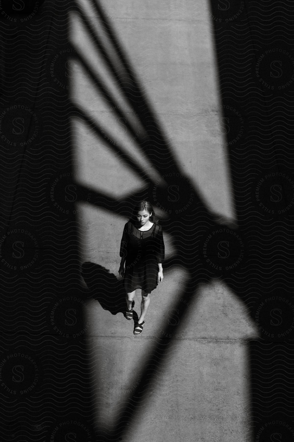 A woman in a black dress walks on a sidewalk under the shadow of a bridge