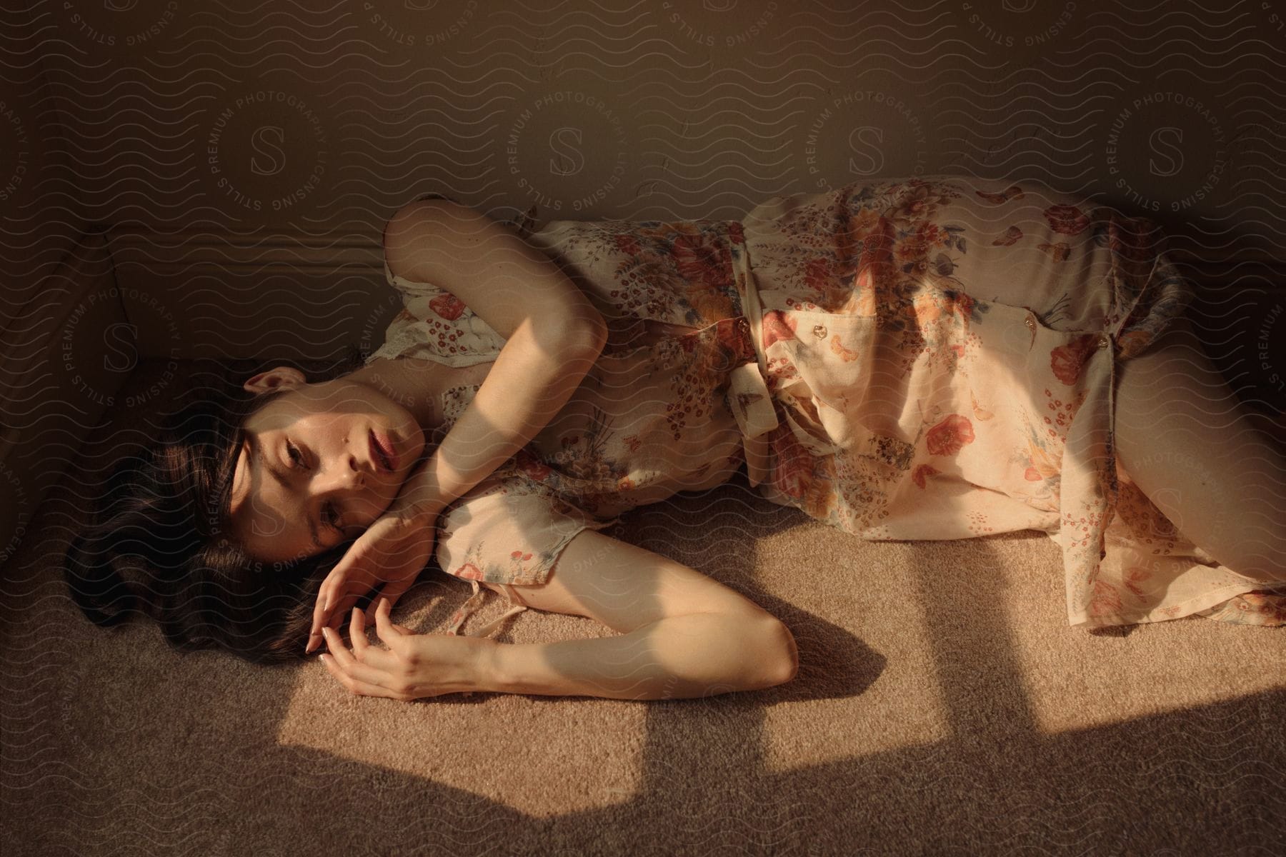 Darkhaired woman wearing a summer dress lying down on the floor over a carpet