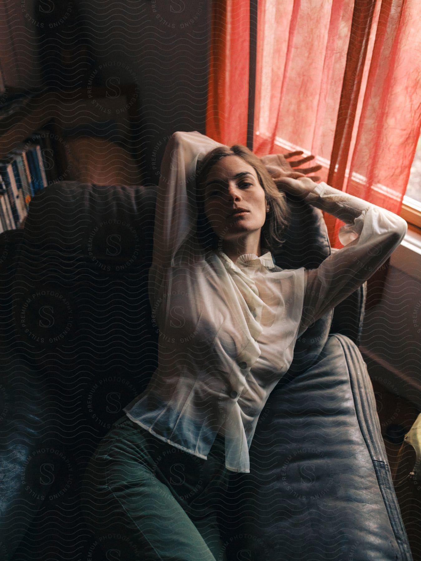 A woman lying down on the sofa wearing a sheer white blouse and denim pants