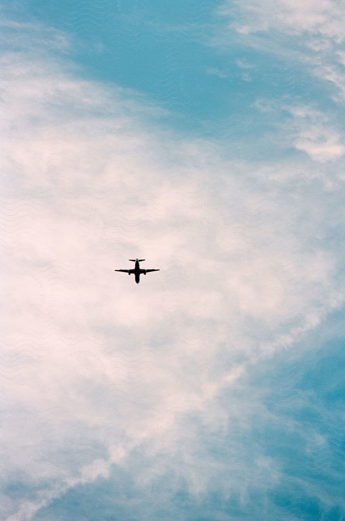 An airplane flying high in a partially cloudy sky