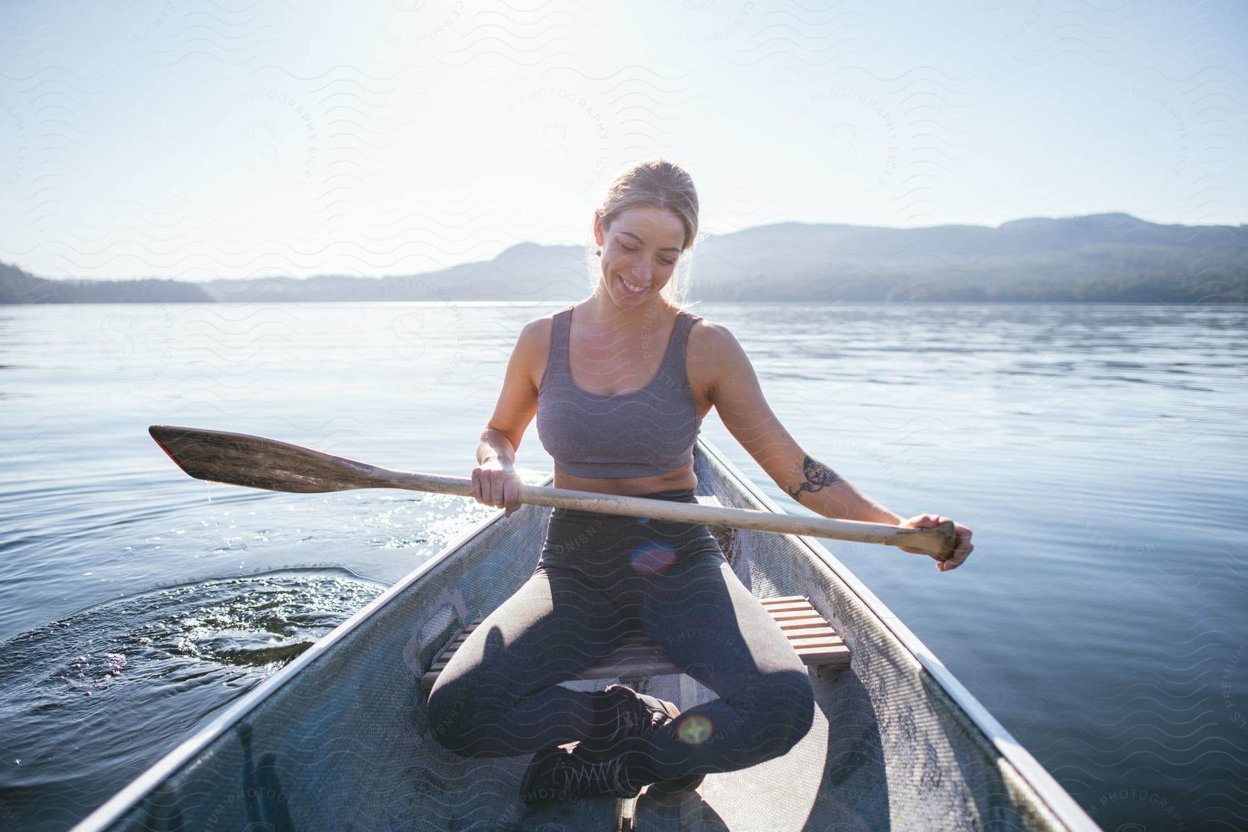 A woman rows a boat in a lake near mountains on a sunny day