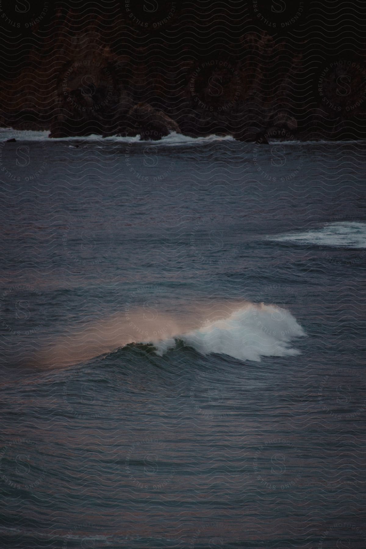 Water splashes and mist rises as waves roll into shore at an exterior location during dusk or dawn in california