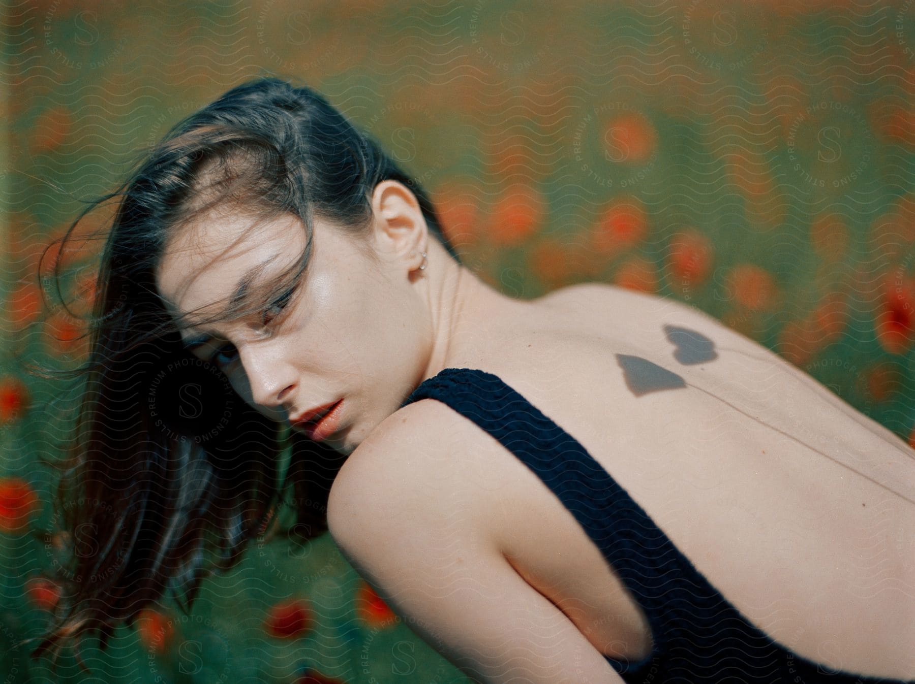 Woman with black dress and flower tattoos poses in red flower field