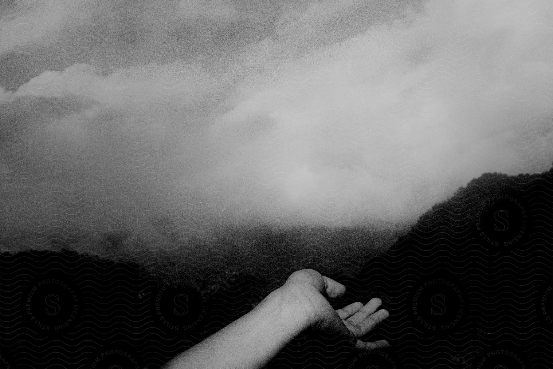 Black and white shot of a human hand gesturing in front of a dark natural landscape covered in fog