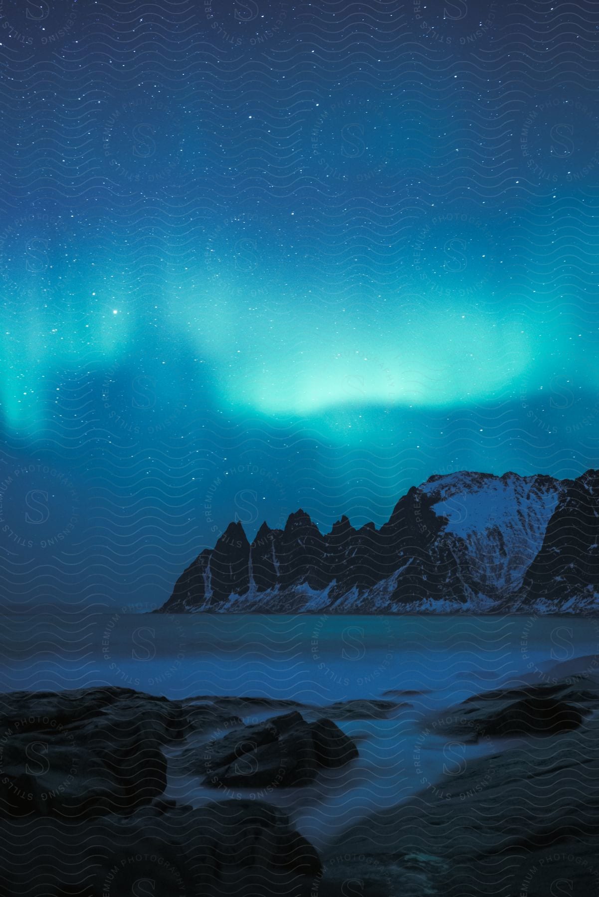 Aurora borealis glows above snowcovered mountains and a frozen lake in a starry night sky