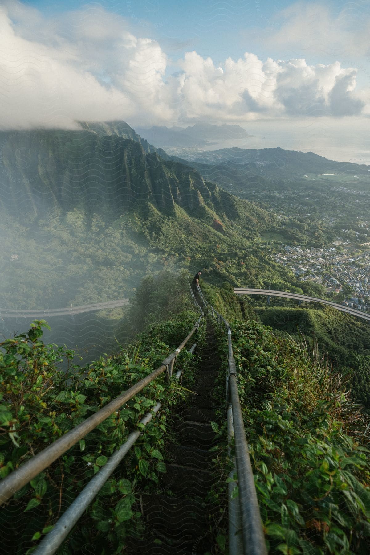 A mountain trail with a railing city highway and mountain range in the background