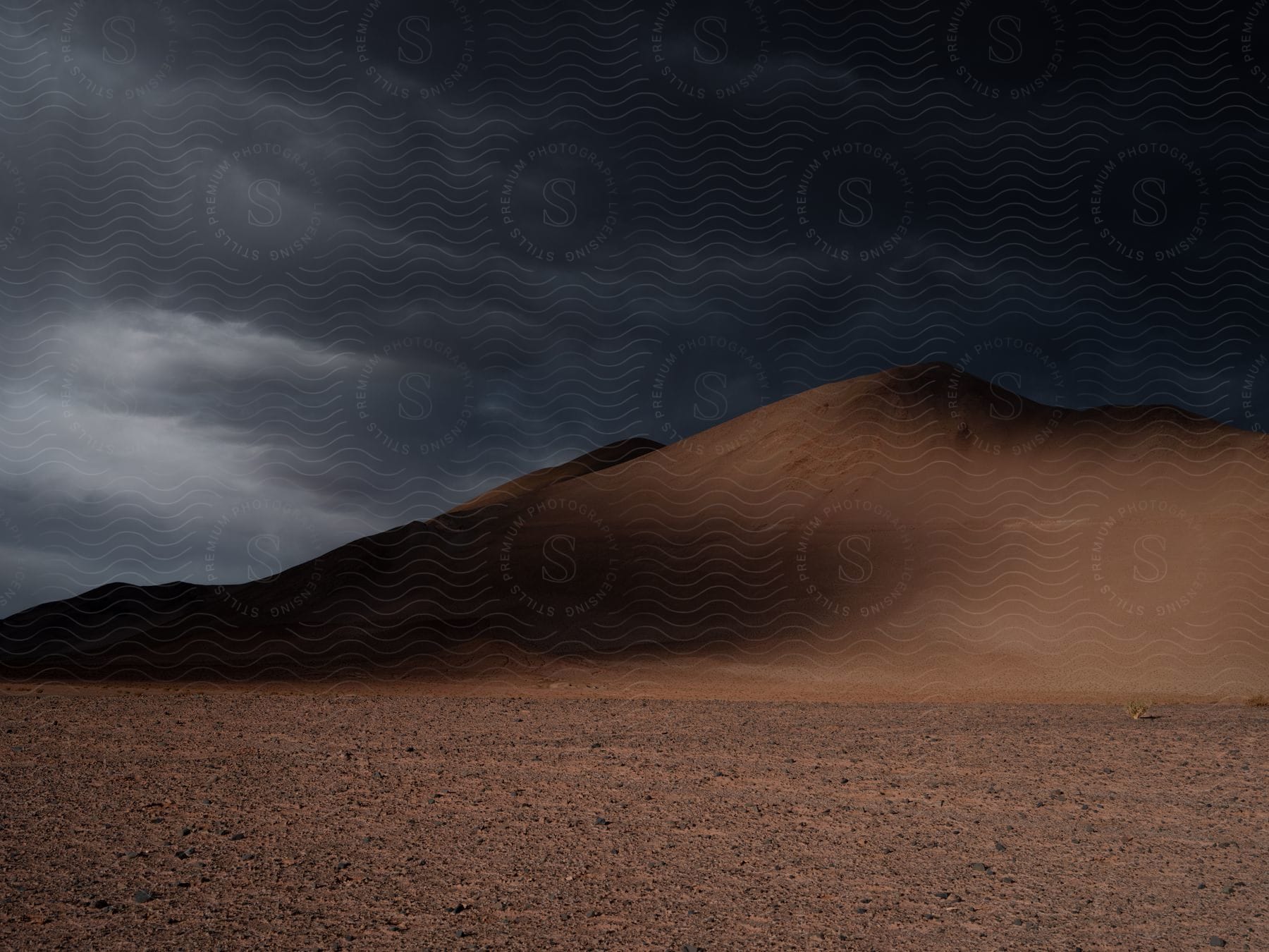 A mountainous landscape with brown ground sky and clouds