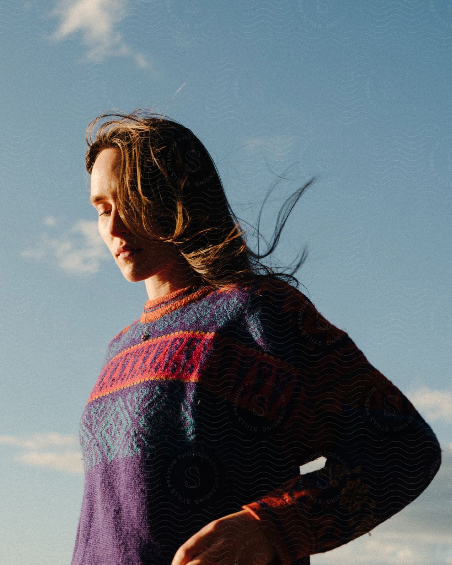 Teenage girl standing outside in a sweater wind blowing her long brown hair as the sun shines upon her