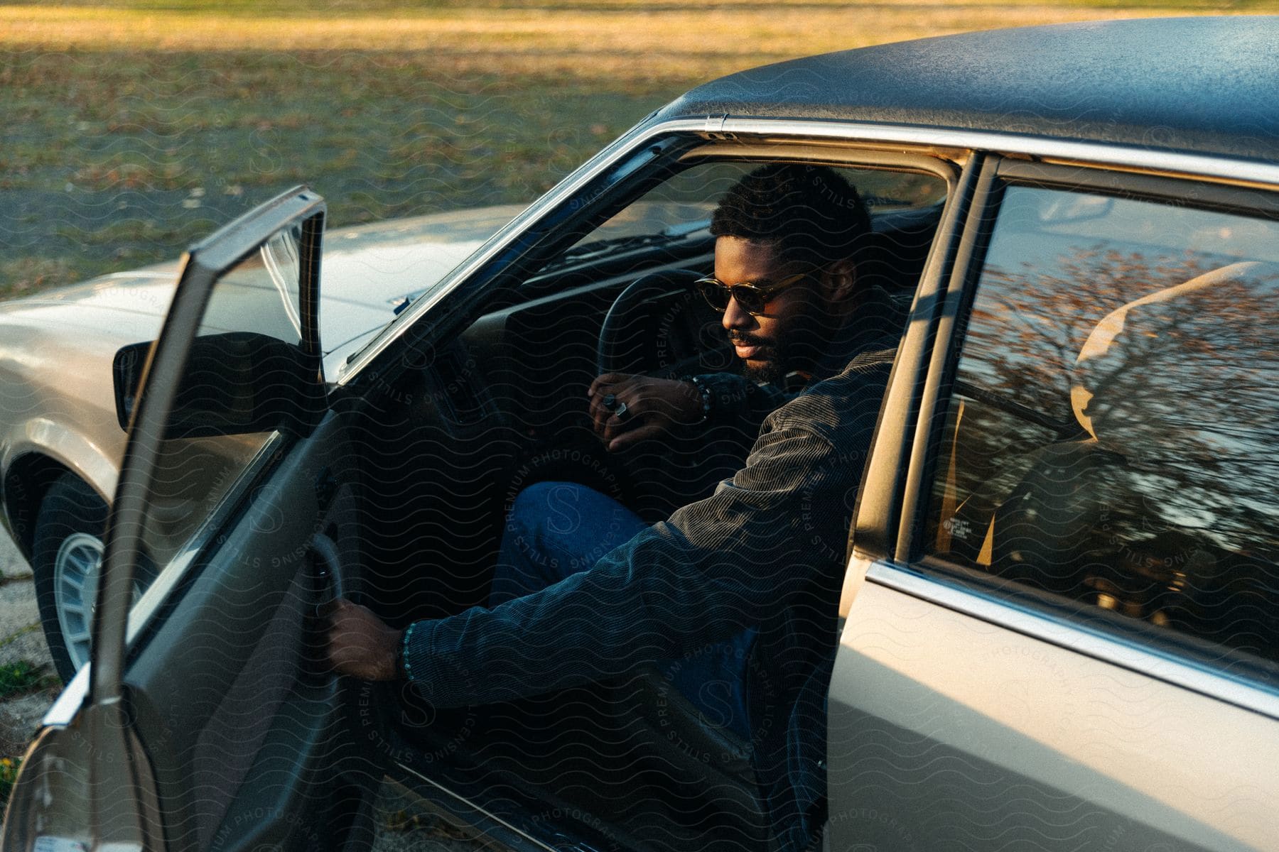 A man sits in a vintage car holding the door open