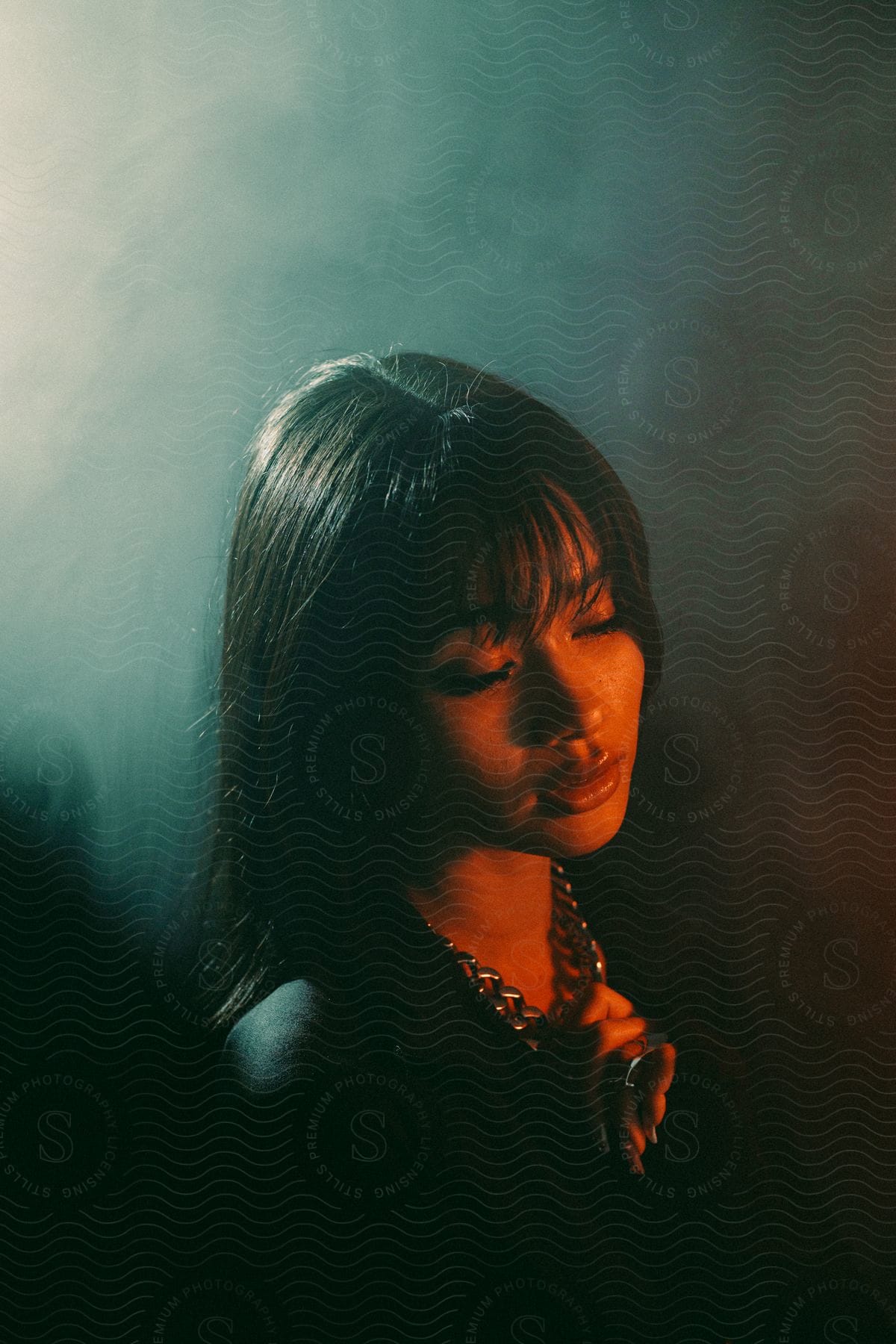 A woman poses with her eyes closed clutching her necklace against a smoky background in a studio shoot