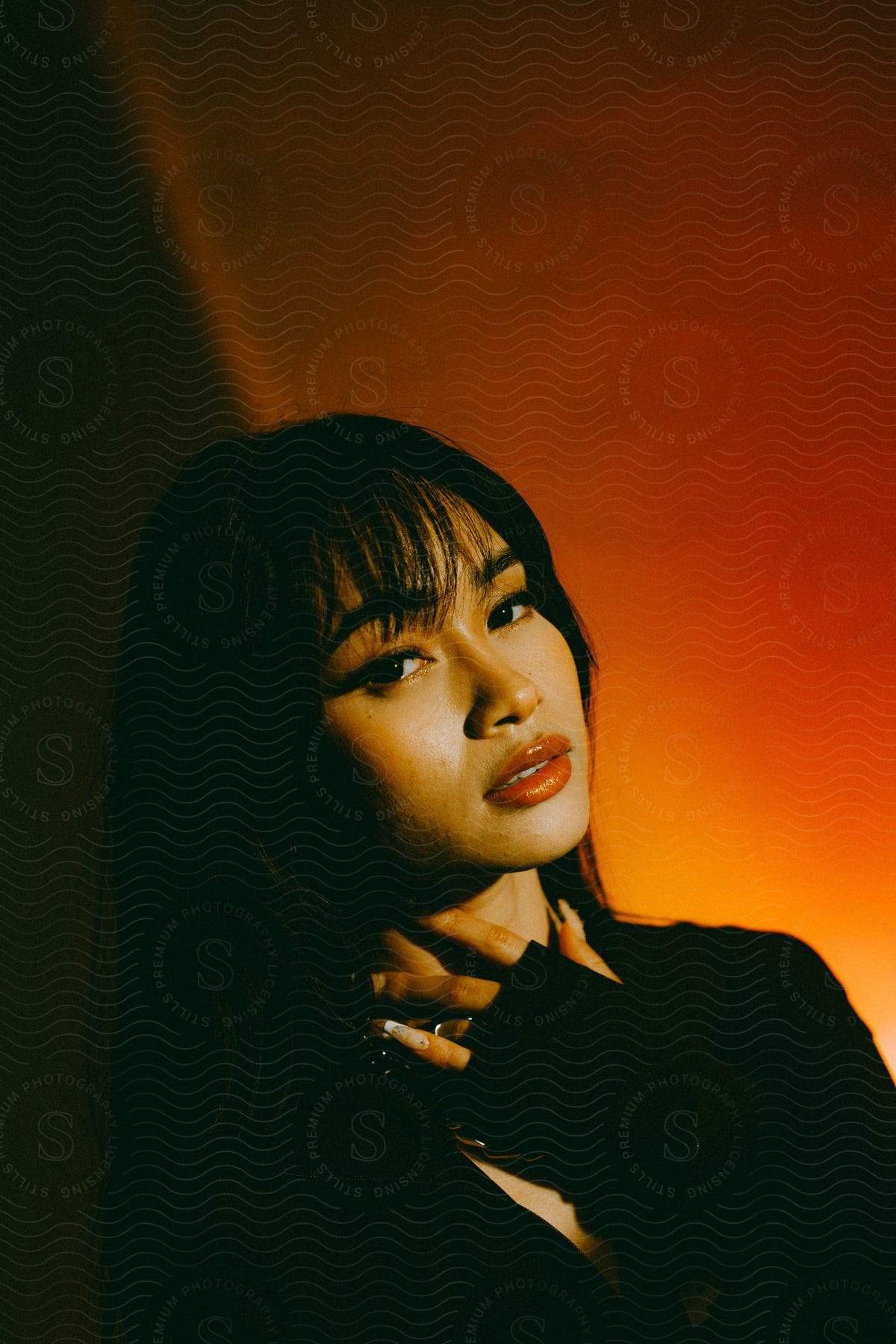 An asian young woman dressed in black poses for the camera in front of an orange wall