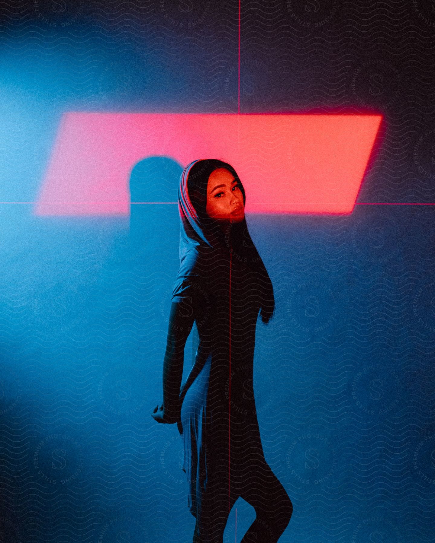 A woman in a hooded dress looks to her right with cross hair lights and a red background contrasting the blue and black lighting