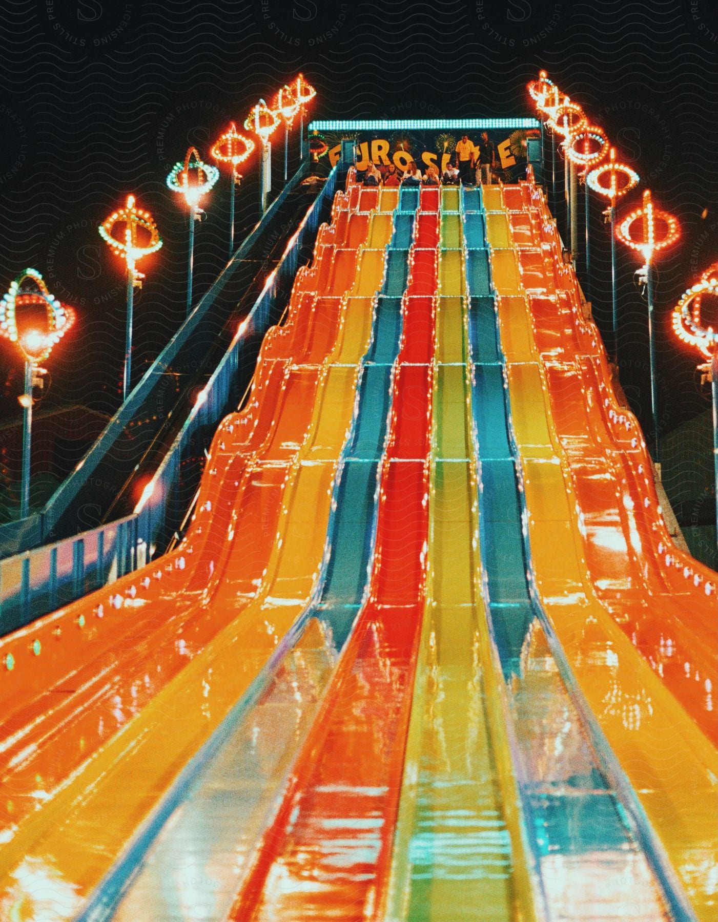 People wait at the top of a tall slide in an outdoor location at night time