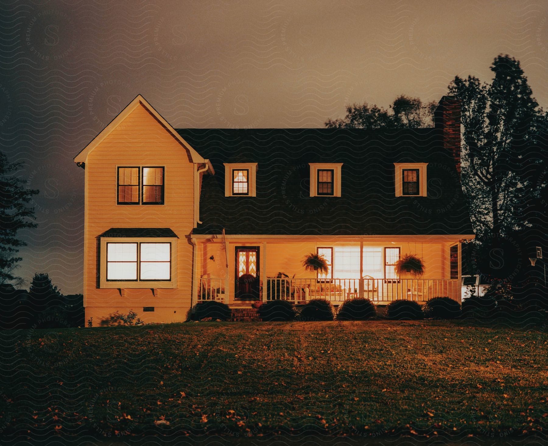 A brightly lit house at night surrounded by trees and grass