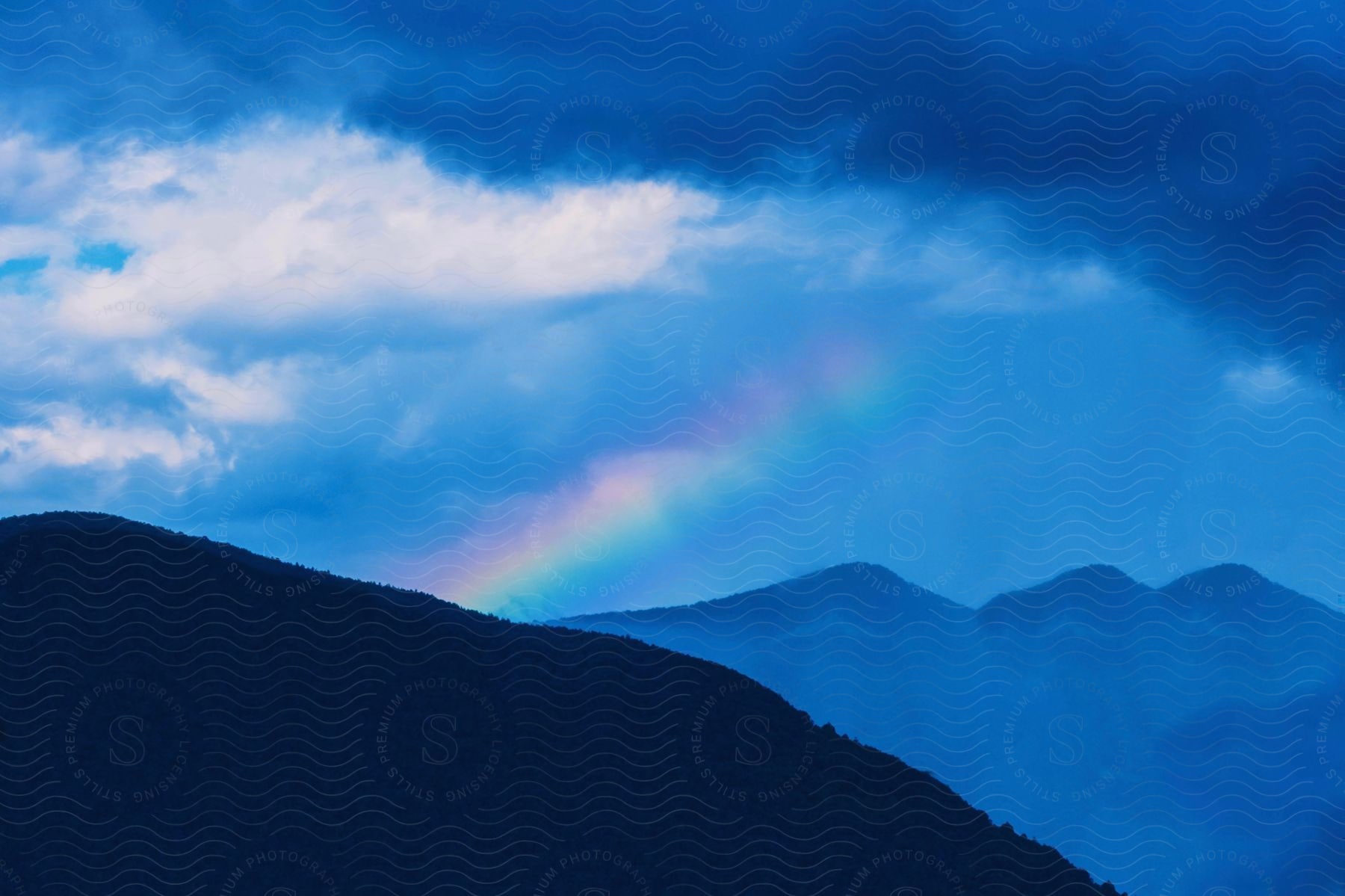 A rainbow over fogcovered mountain range under a dark clouded sky