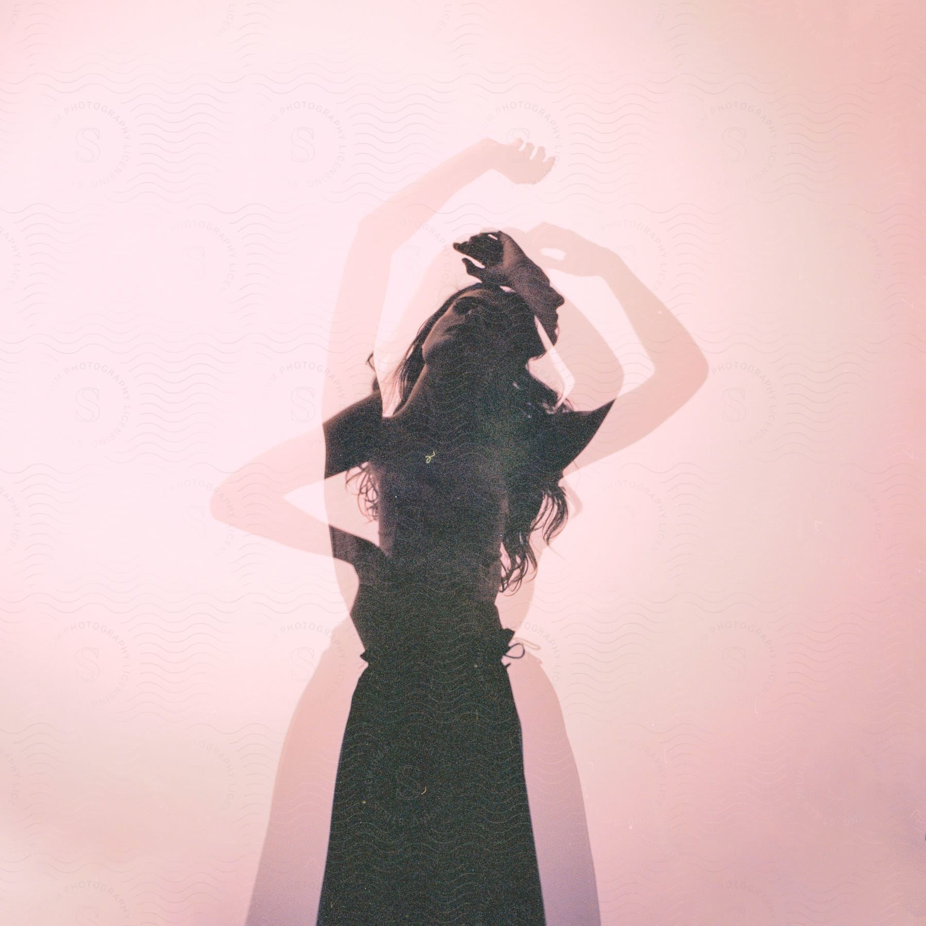 Woman in silhouette performing a dancelike movement against a pink background in a double exposure image