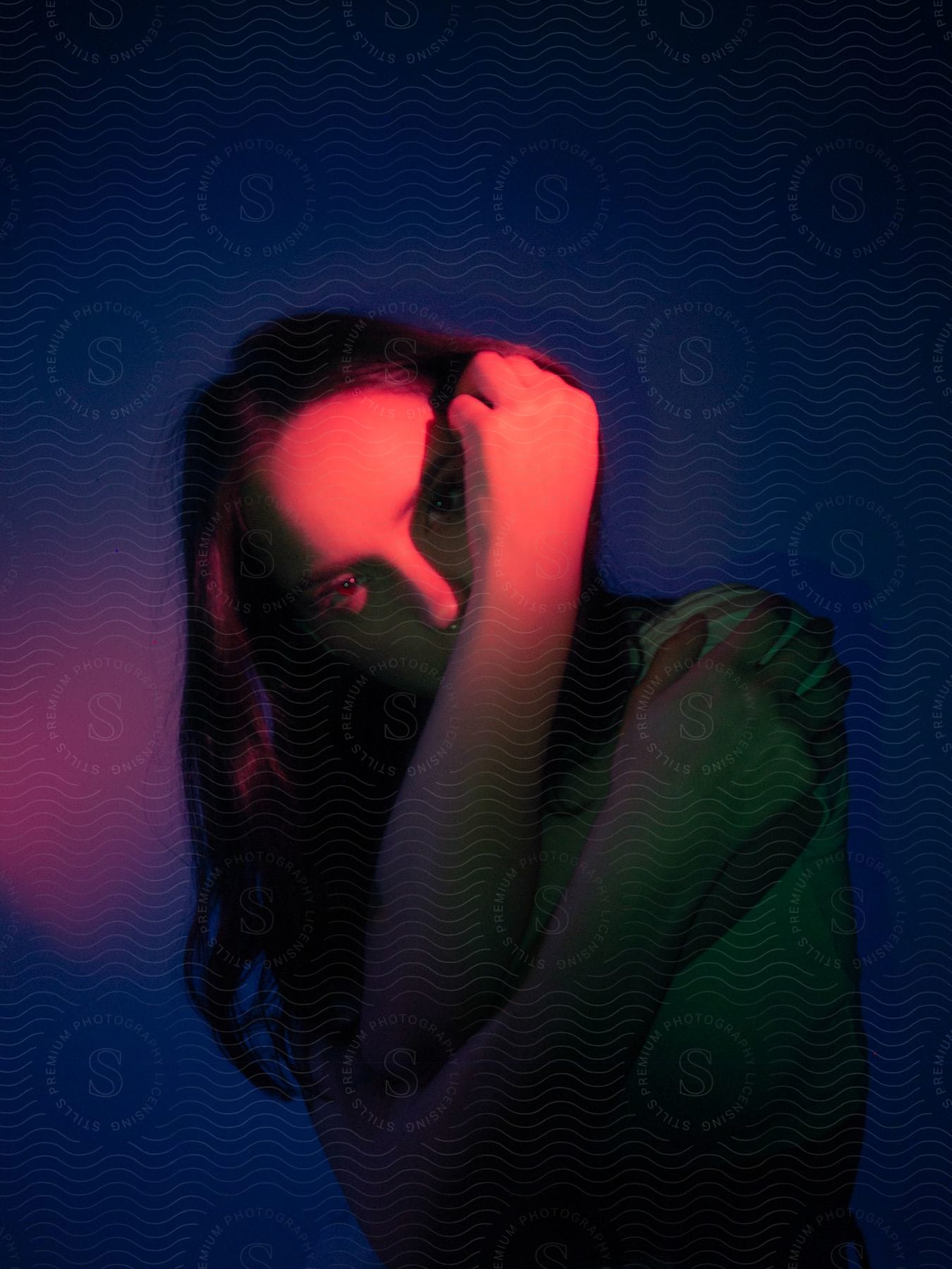 A woman wraps her arms protectively around herself, her face emerging into the glow of a red light