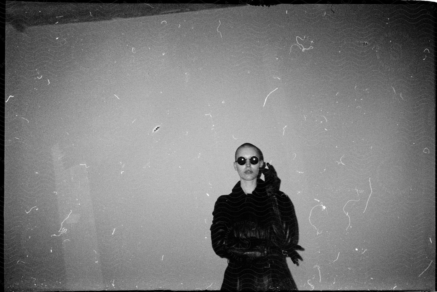 woman with shaved head sunglasses black gloves and leather jacket poses for the camera