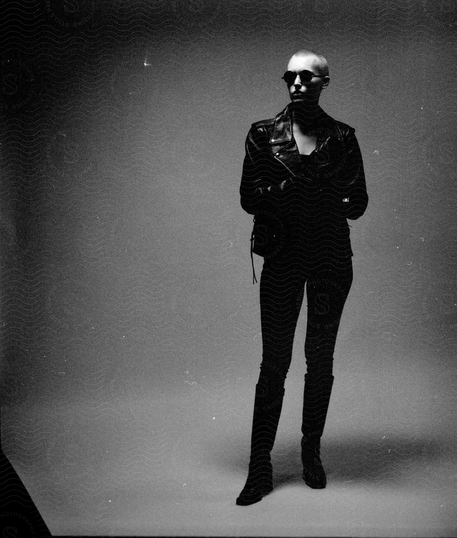 a model stands in a leather jacket and sunglasses indoors