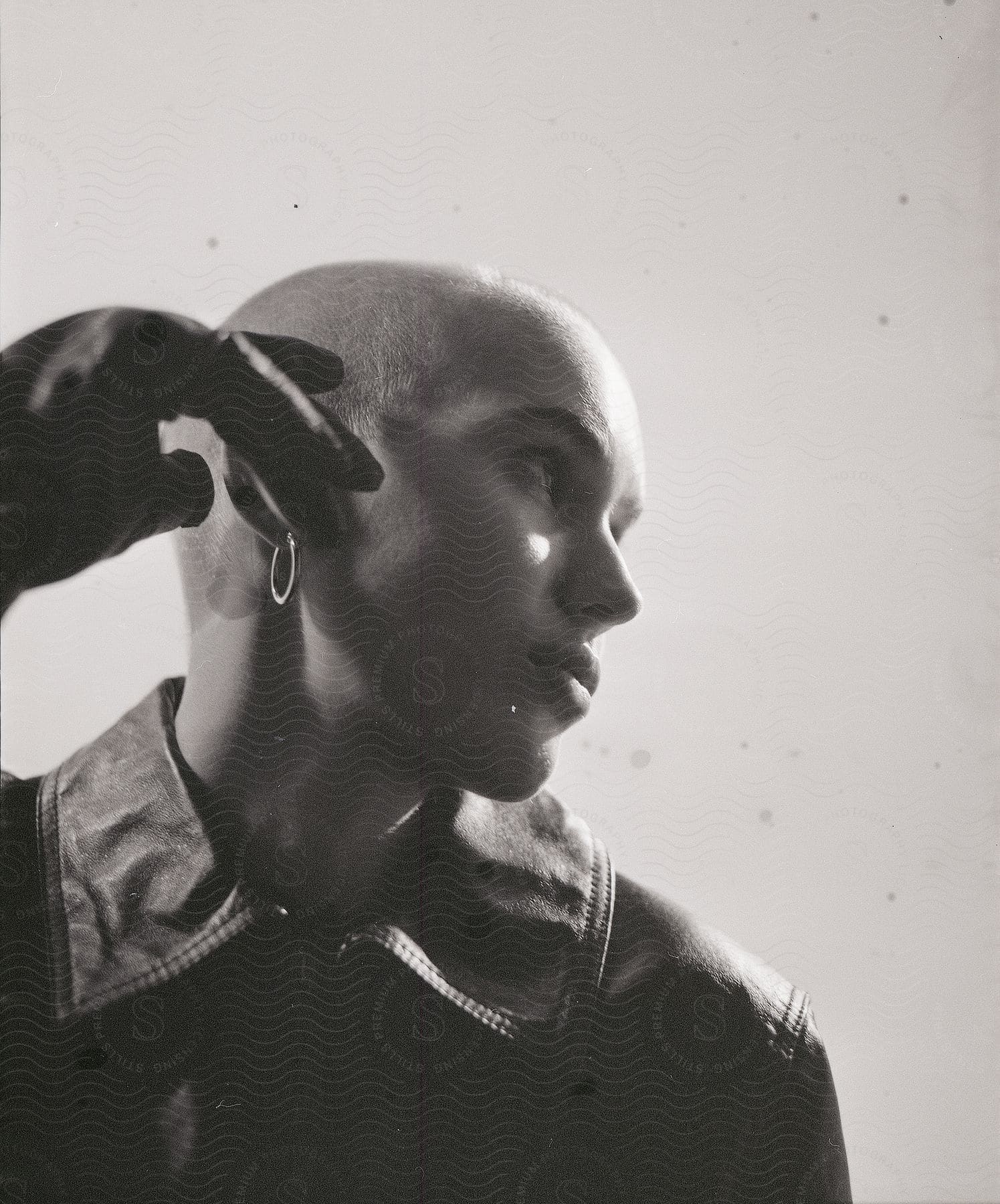 Woman with shaved head and black leather jacket looks away