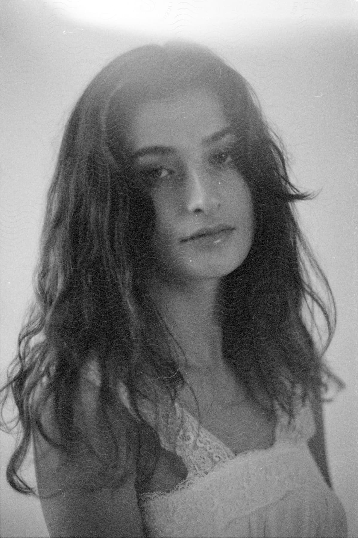 A young woman with long brown hair faces the camera wearing a sleeveless white nightgown.