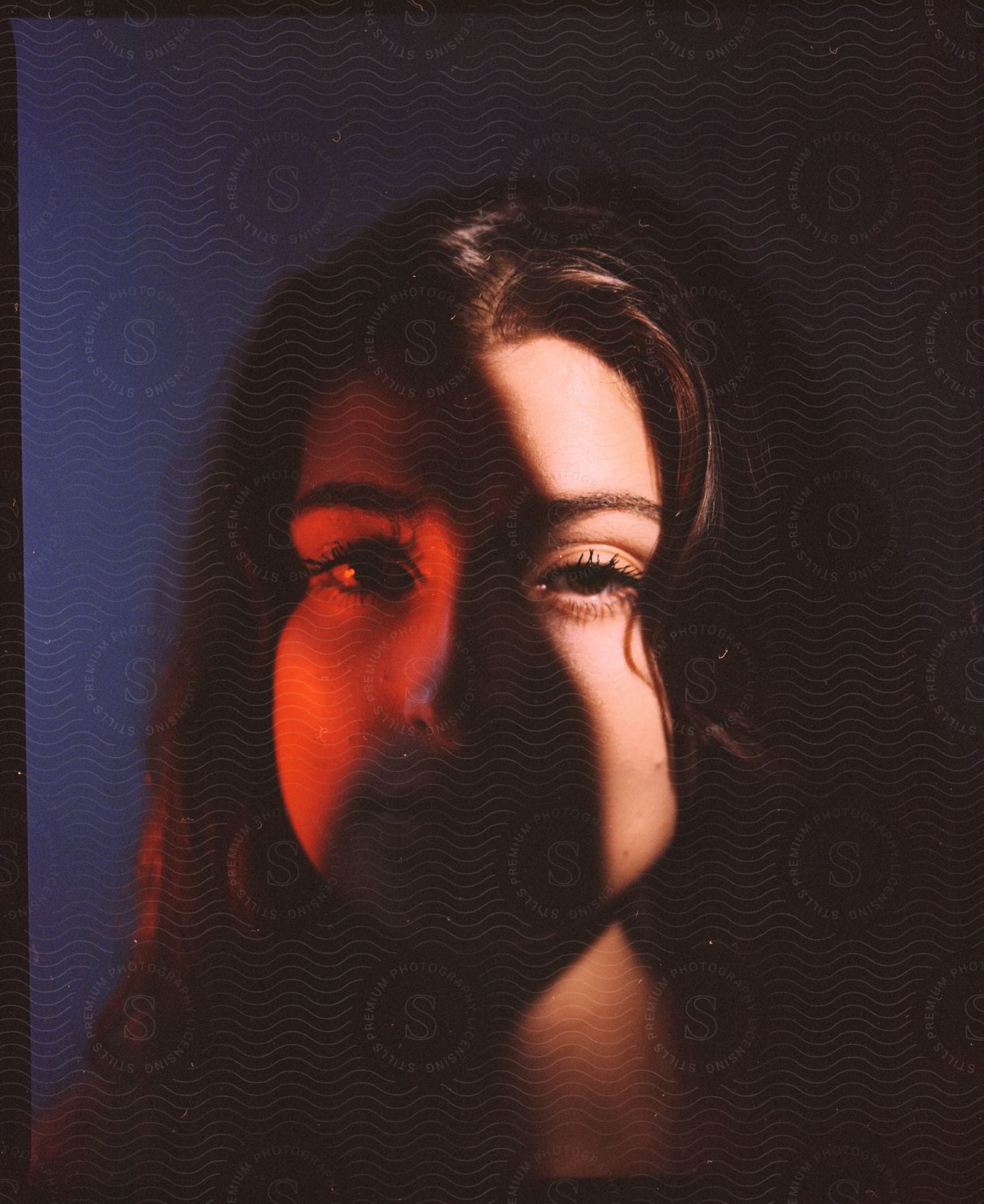 A young woman with long, brown hair poses while orange and natural light highlight her face.