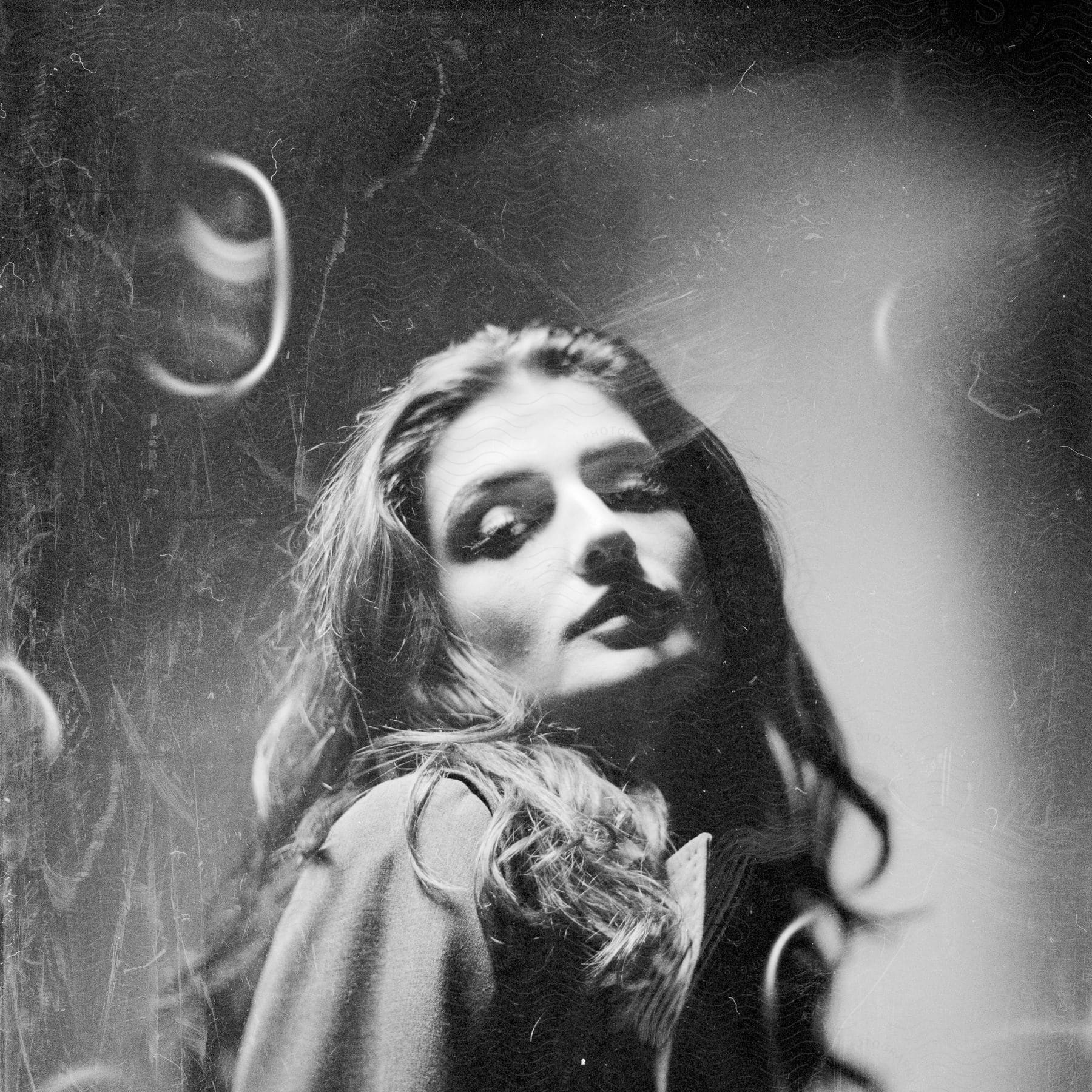 Close-up of a woman with wavy brown hair, looking down and smiling, captured in a tattered photograph.