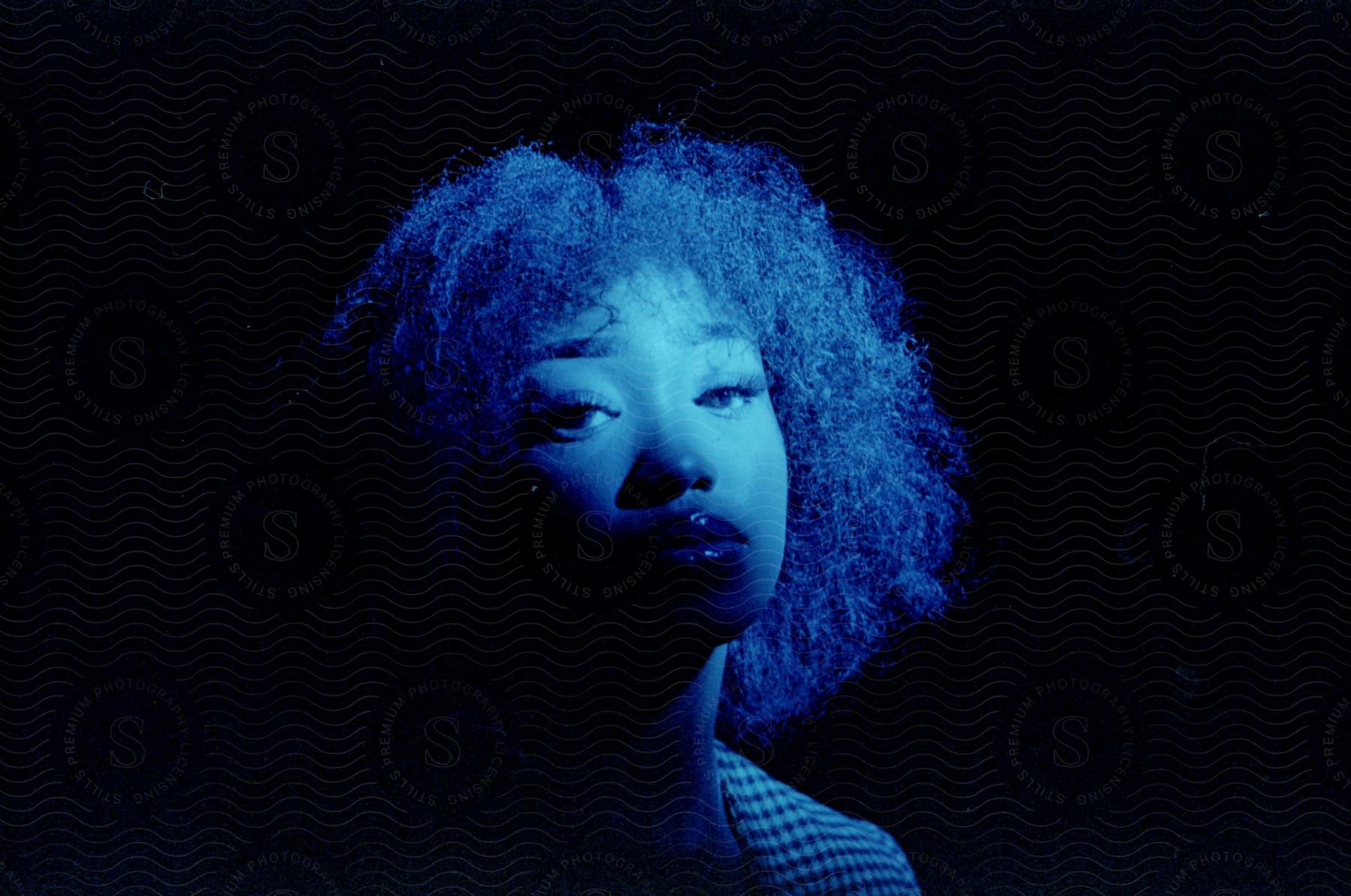 Black woman with afro hair wearing a jacket standing under blue lights