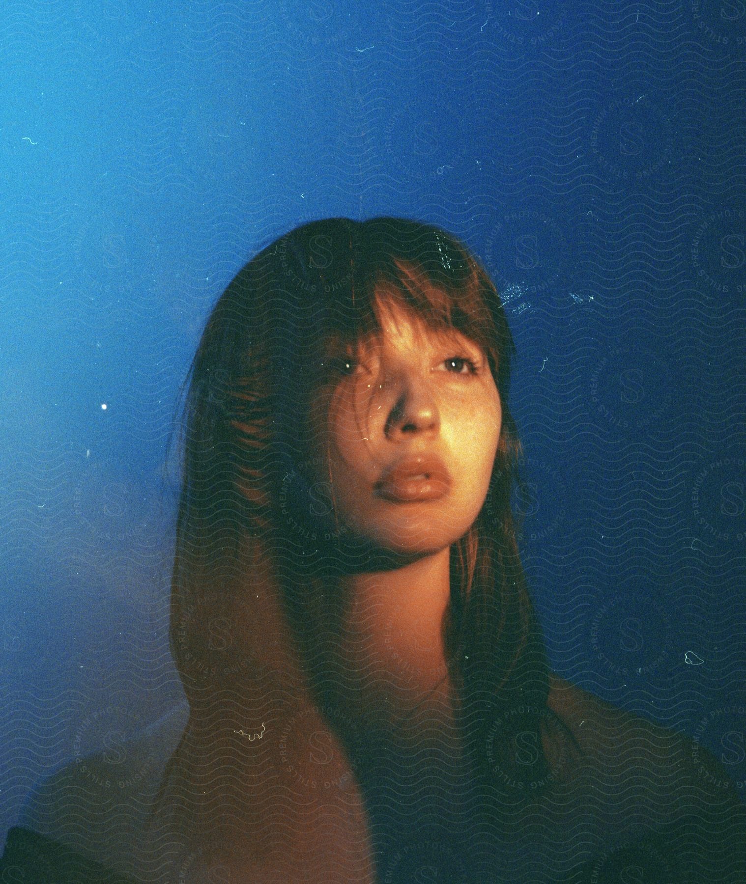 Woman with necklace looks into space while light shines on her face