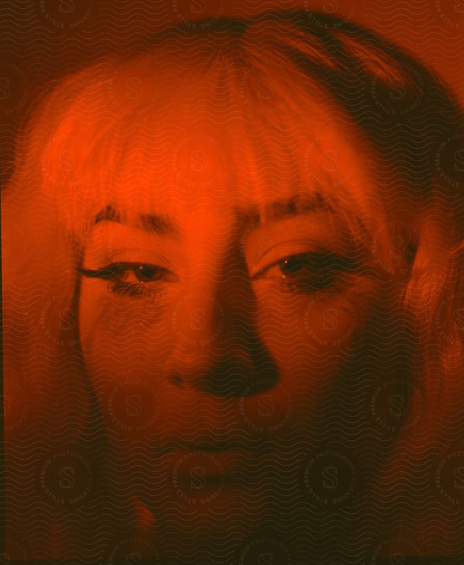 A woman with long black eyelashes and a blonde wig bathed in orange light