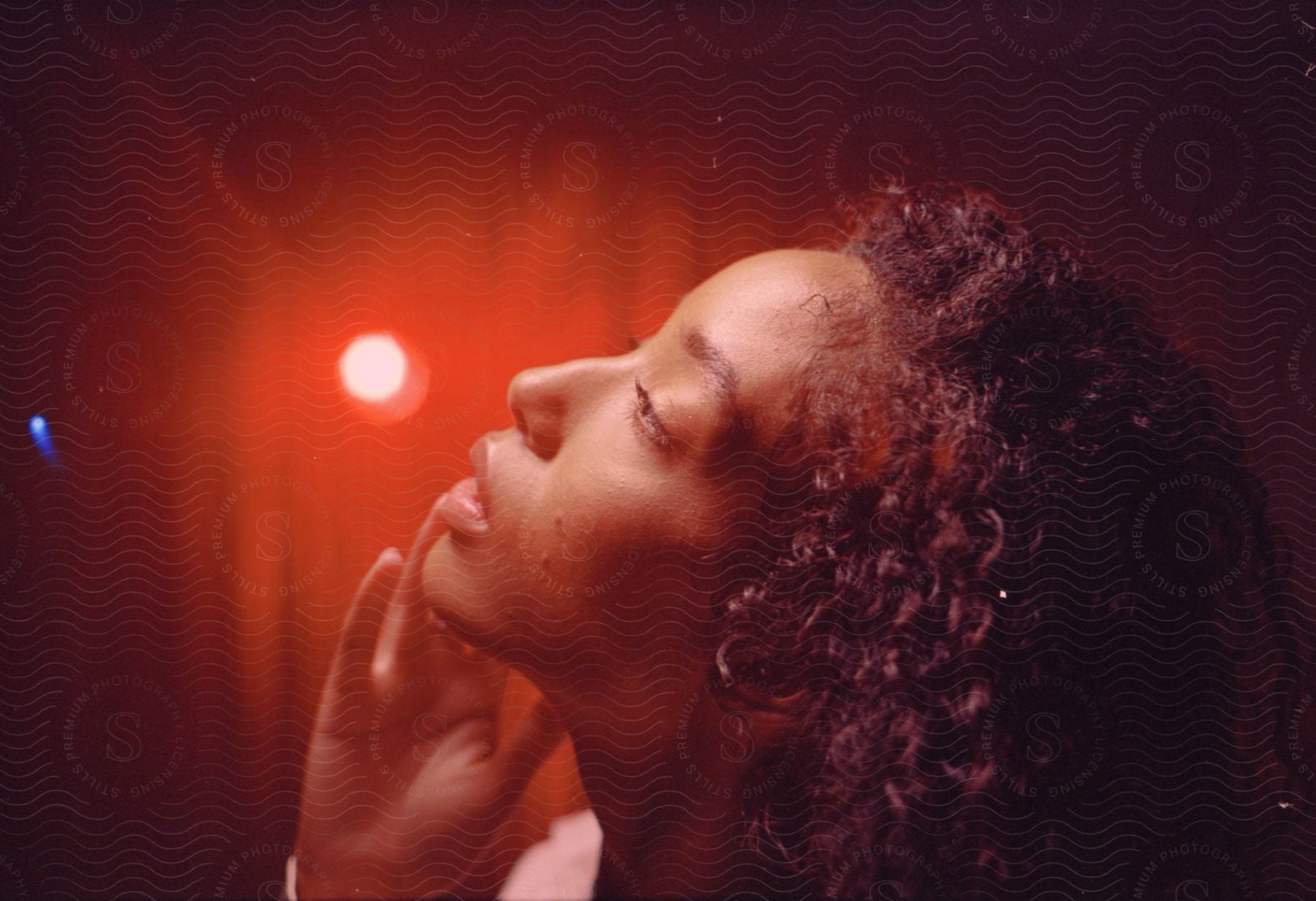 Close up of woman’s face with curly hair in red lighting touching her cheek