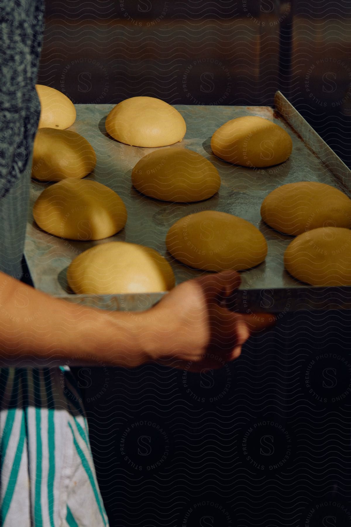 Woman carrying a baking tray of uncooked bread dough in a commercial kitchen