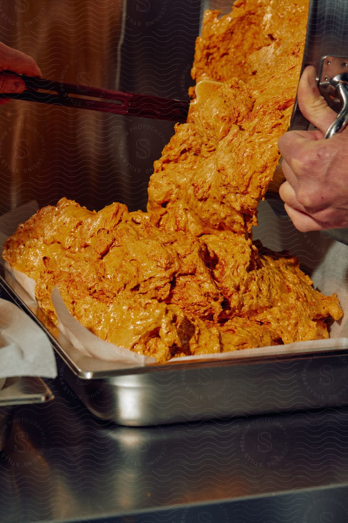 Someone pours vibrant yellow food paste into a large plate in a culinary scene