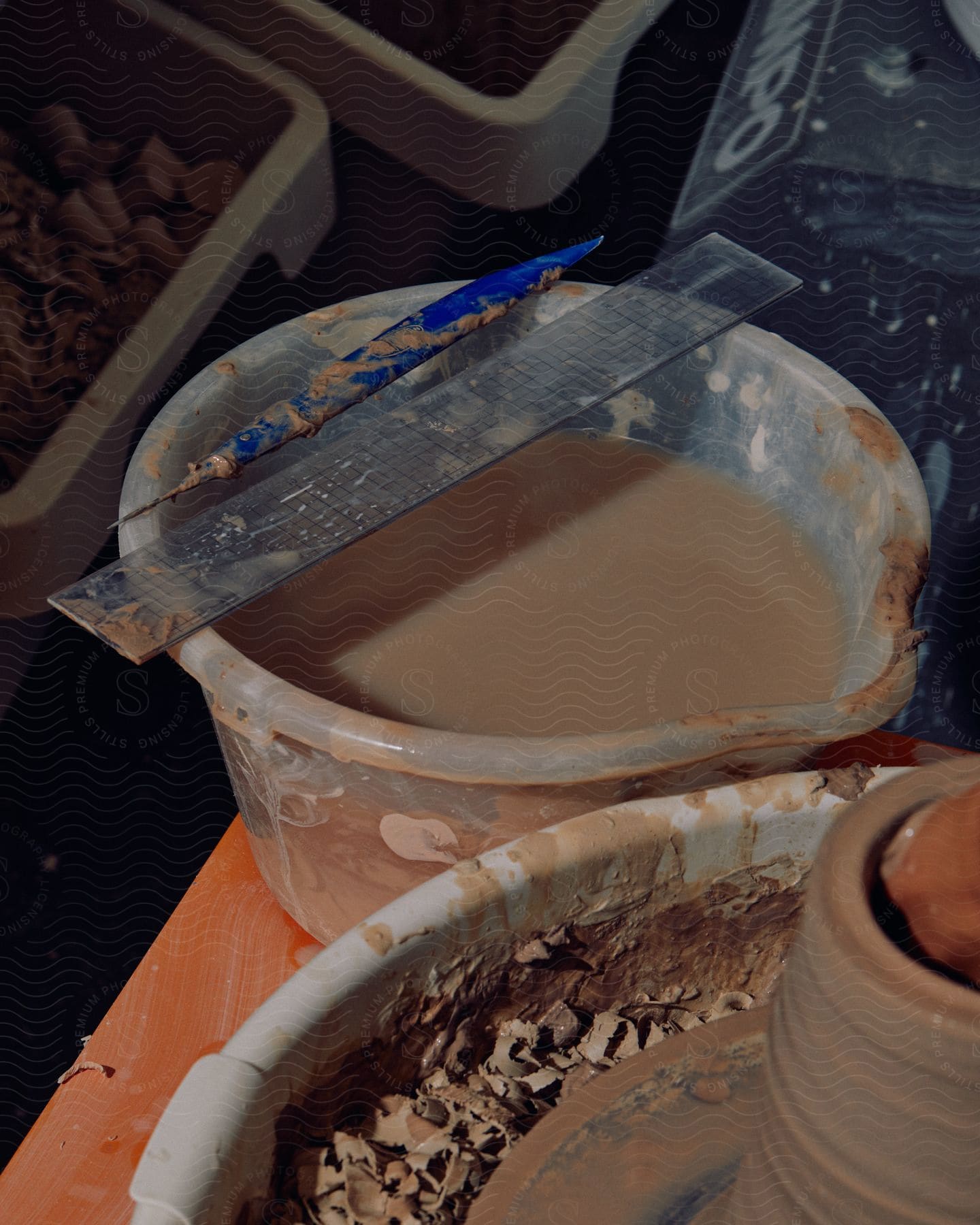 A bucket of water and sculpting tools are next to a potters wheel