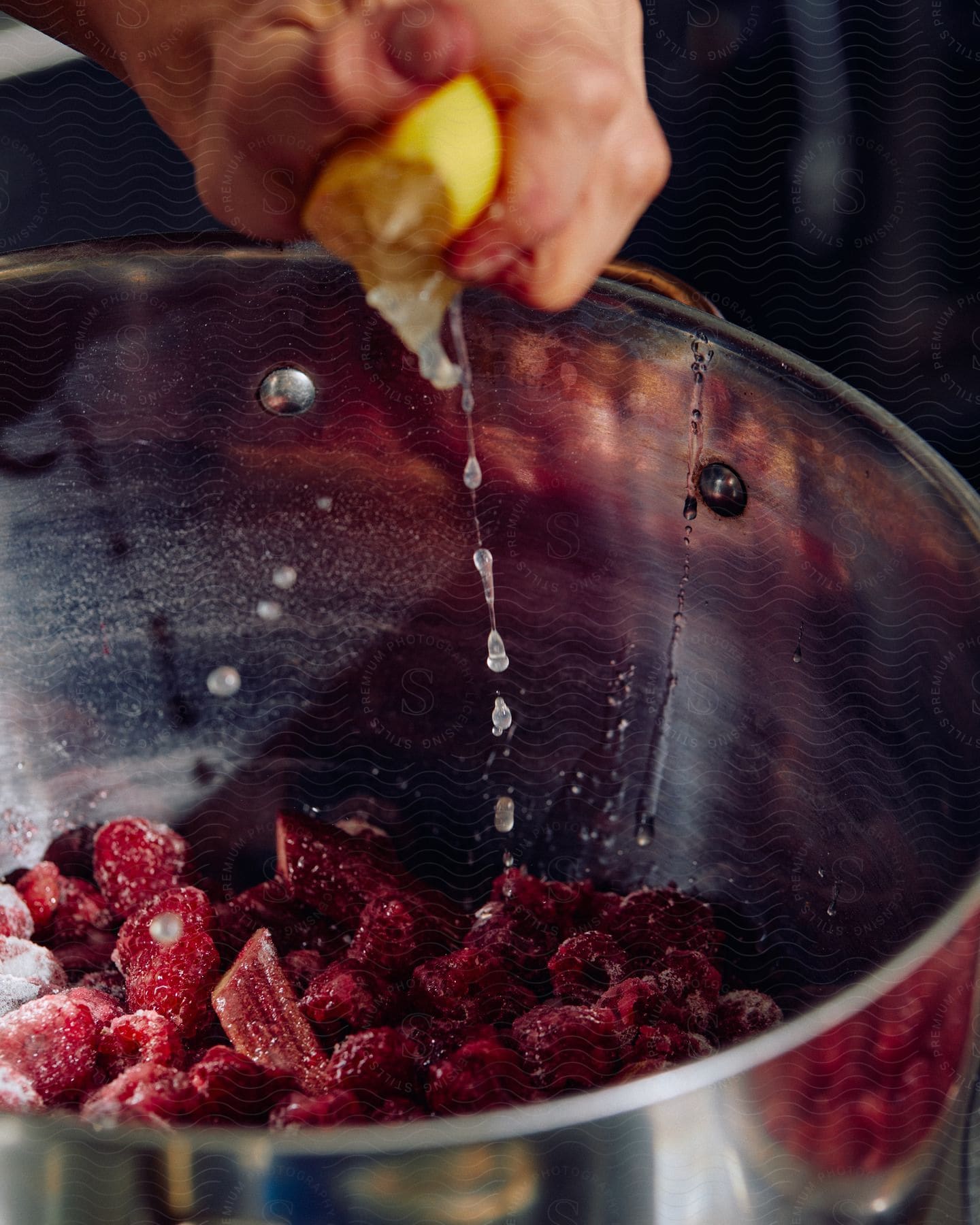 Persons hand in a kitchen squeezing lemon over a pan filled with berries