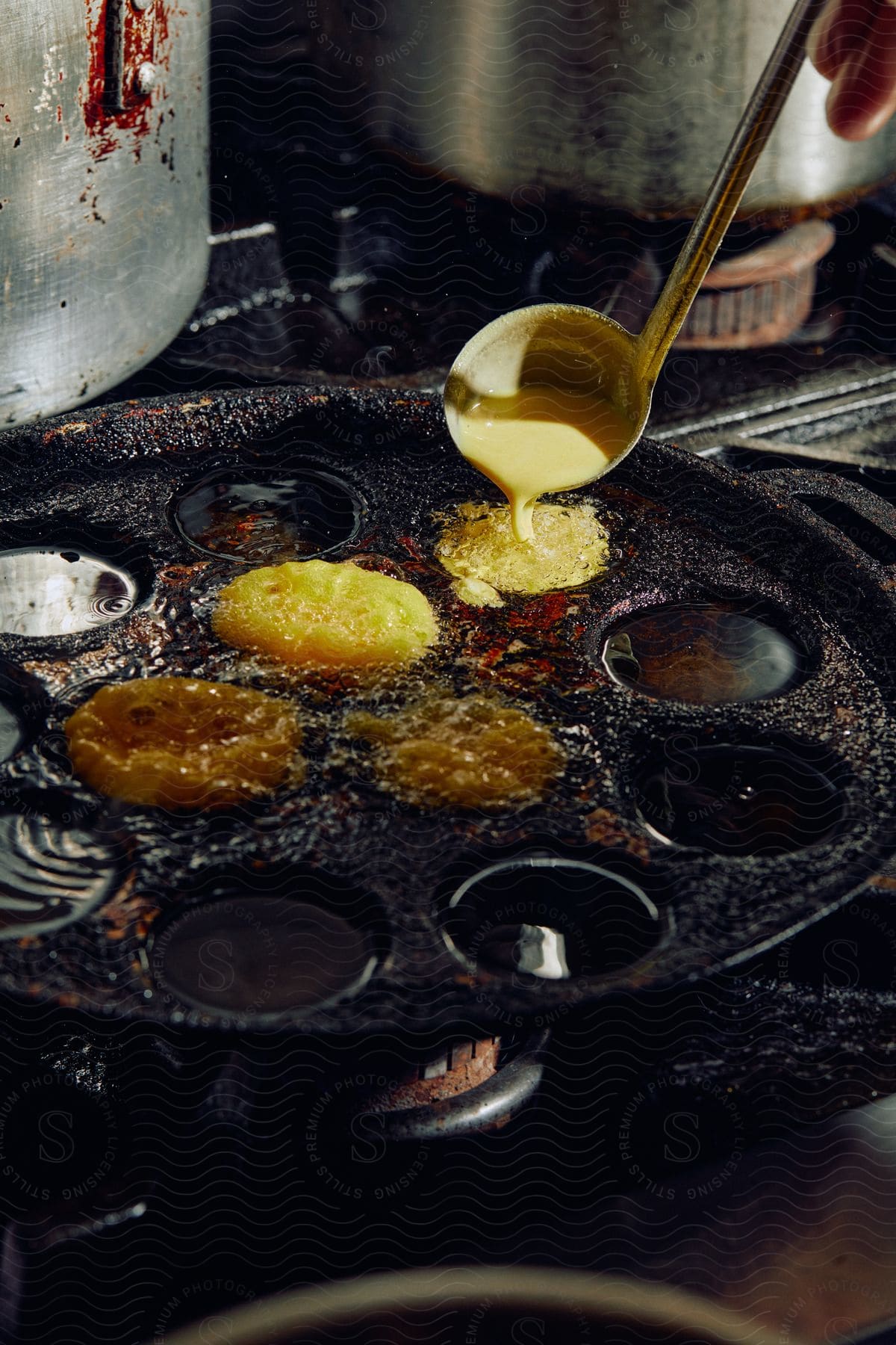 A person using a spoon to drop liquid paste in a pan for cooking