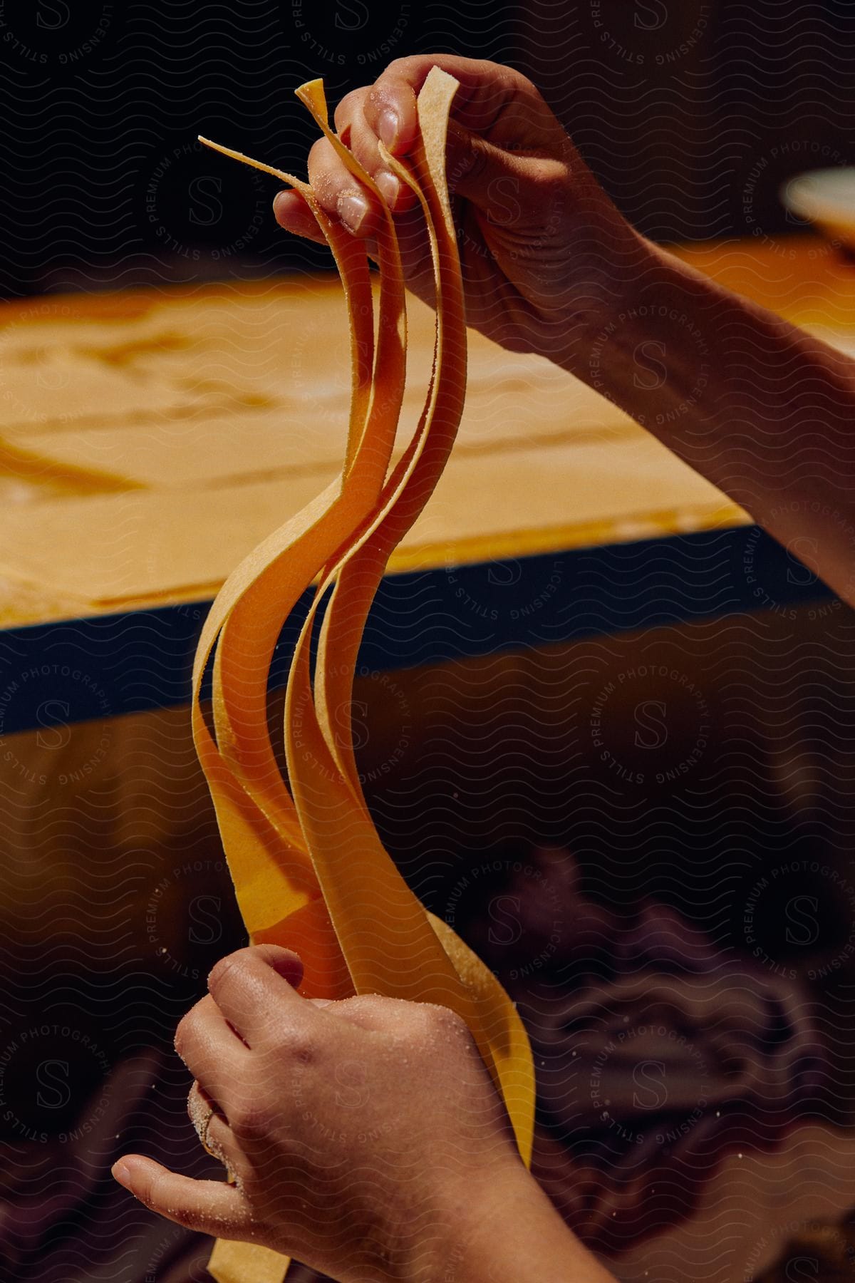 Stock photo of close up of a chef shaking long thick strings of pasta in a kitchen