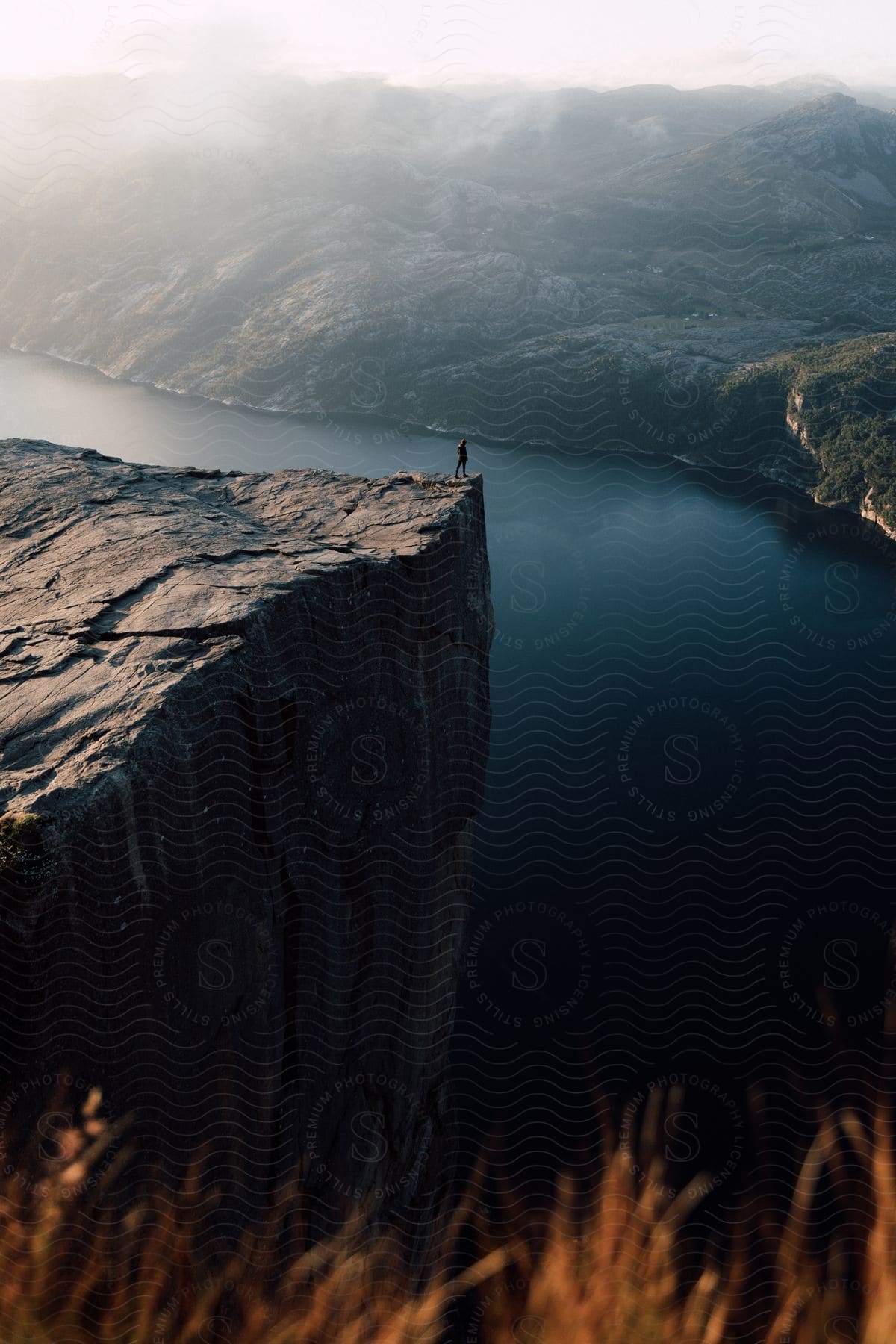 A person stands on a cliff overlooking a lake surrounded by mountains in norway