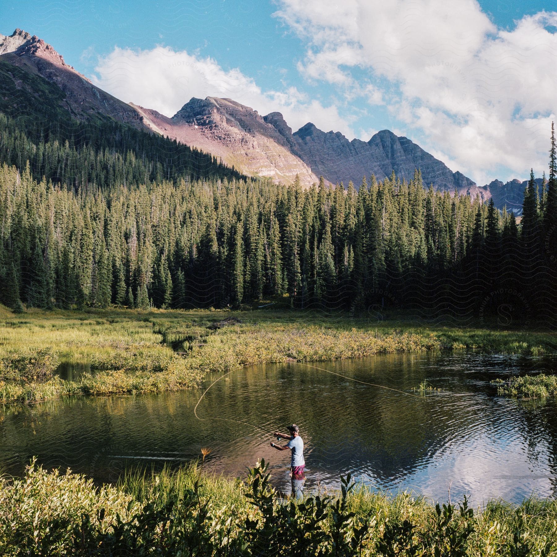 A man fishing in a lake surrounded by trees and mountains in the background