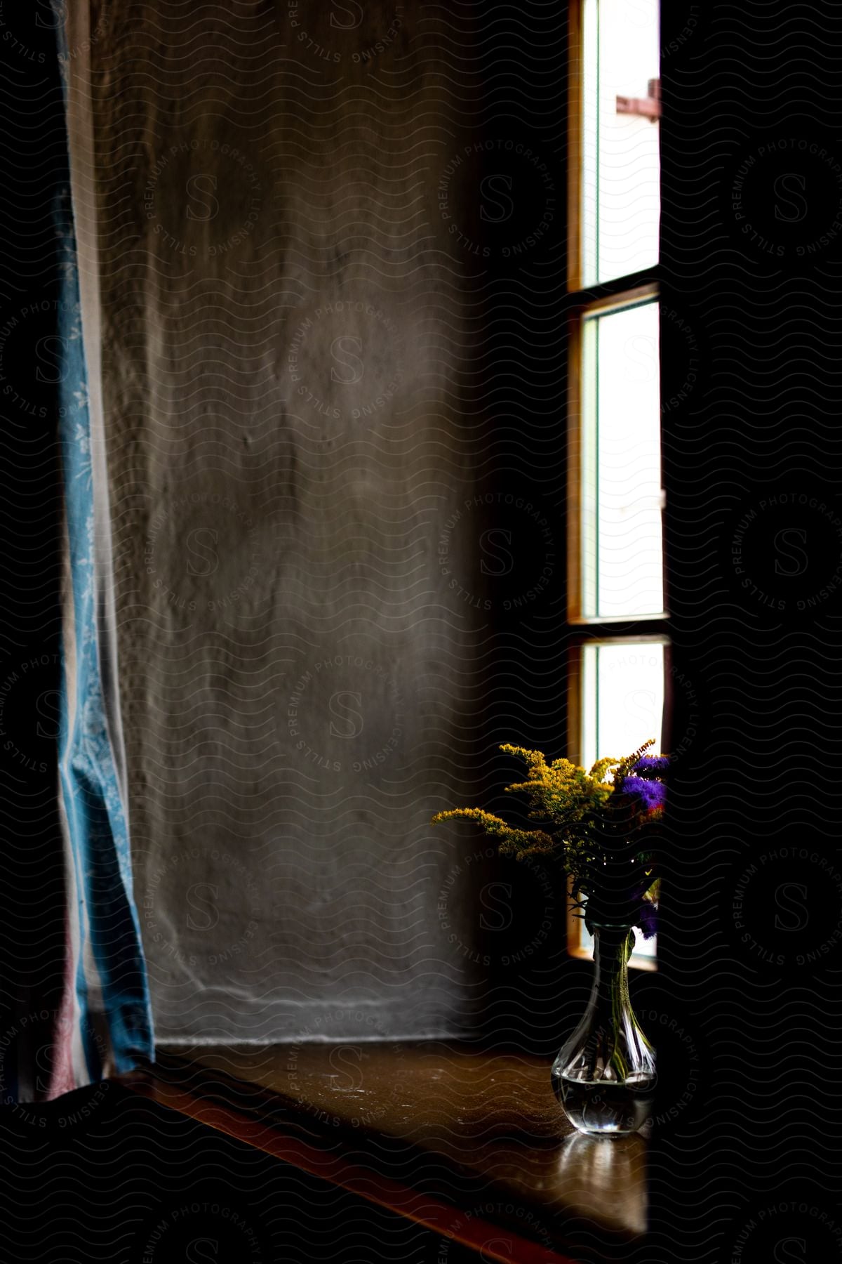 A vase of flowers sits on a windowsill in front of a window with sunlight shining through