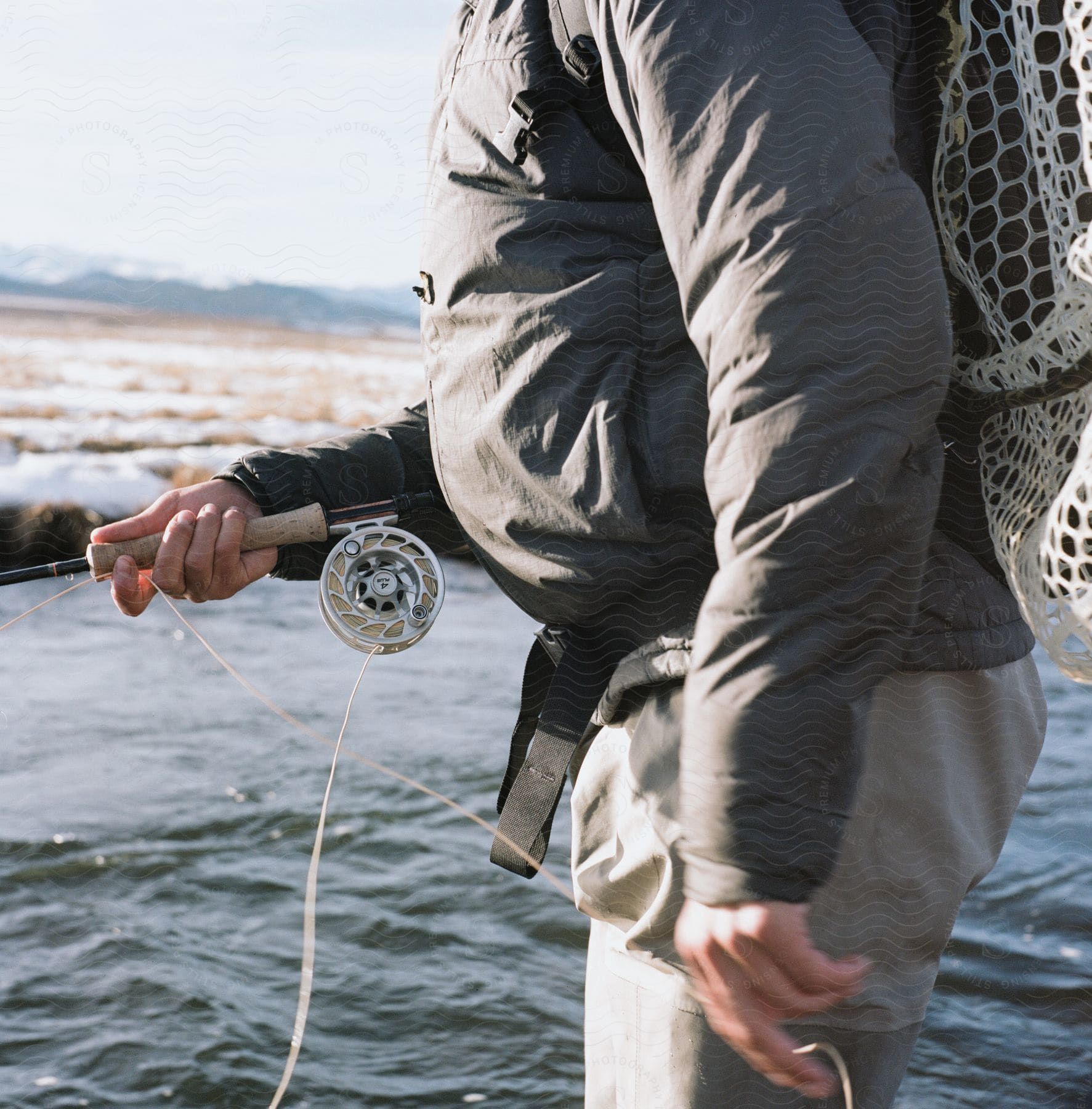 A man fishing in a river near a snowy bank