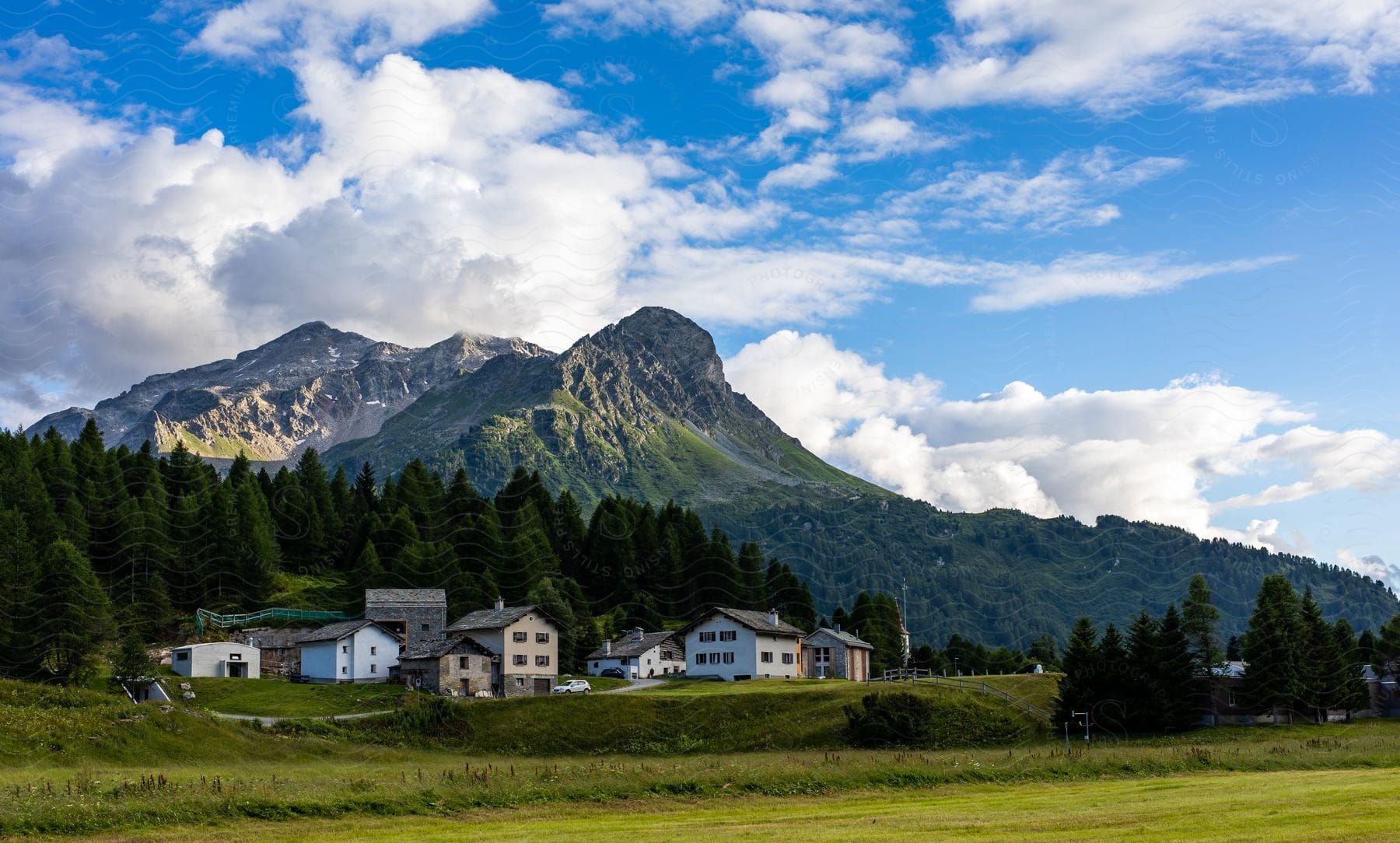 Village nestled in valley with rolling hills grasslands and mountain range on cloudy day