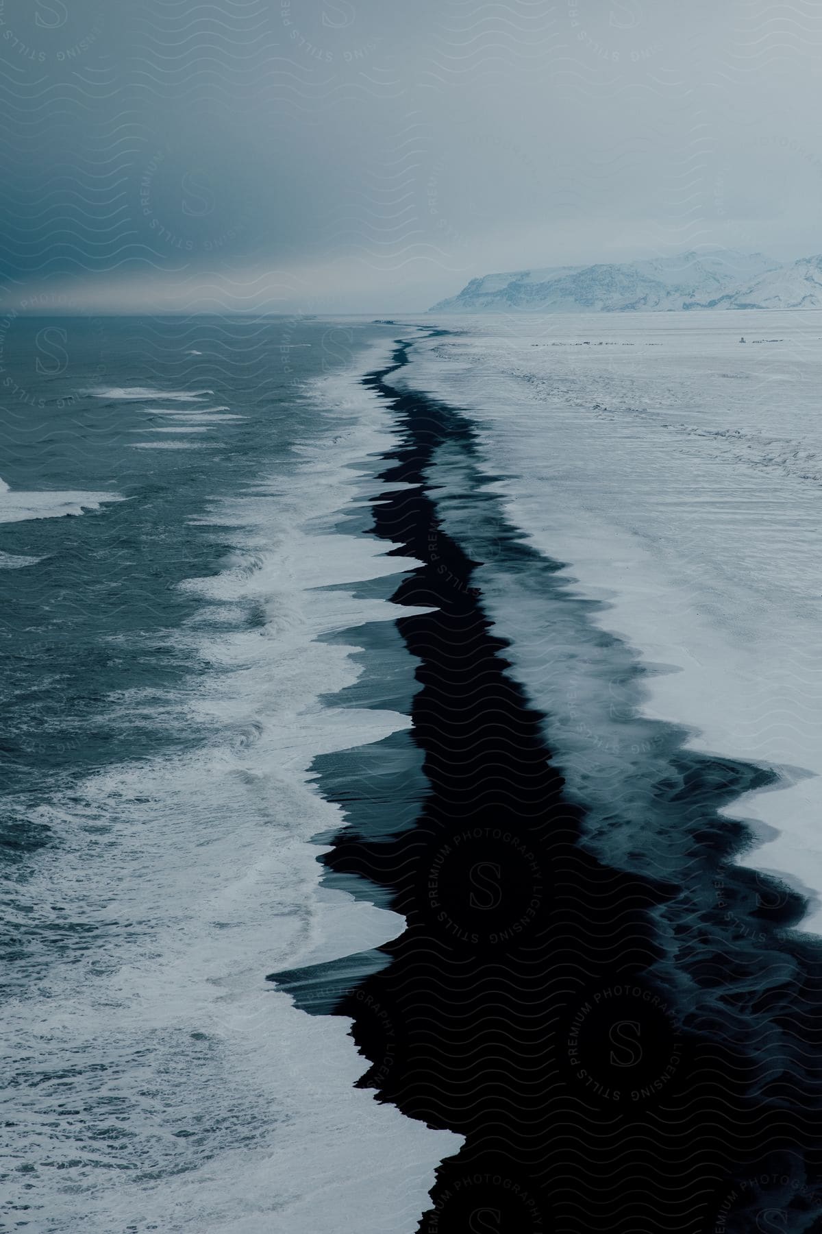 Waves crash on an icy shore with mountains in the background